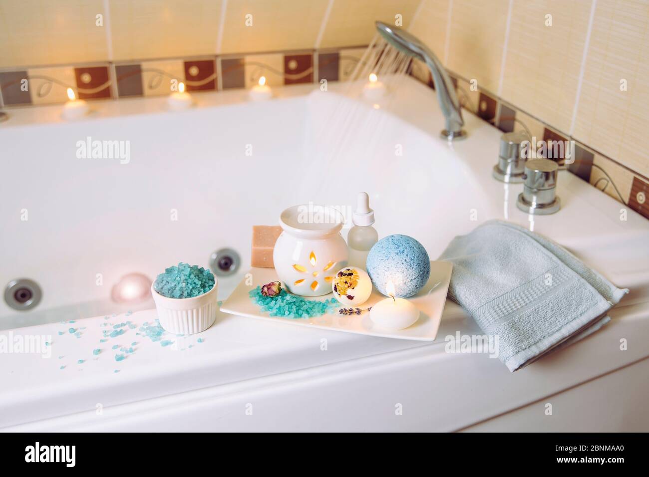 Indoors home spa toiletries on tray in bath room on bath. Ready to spend relaxing alone self time. Blue bath salt bomb and towel. Stock Photo