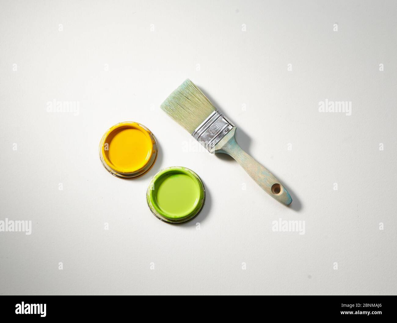 User and washed out wooden brush with two lids of paint cans, yellow and green on a white background Stock Photo