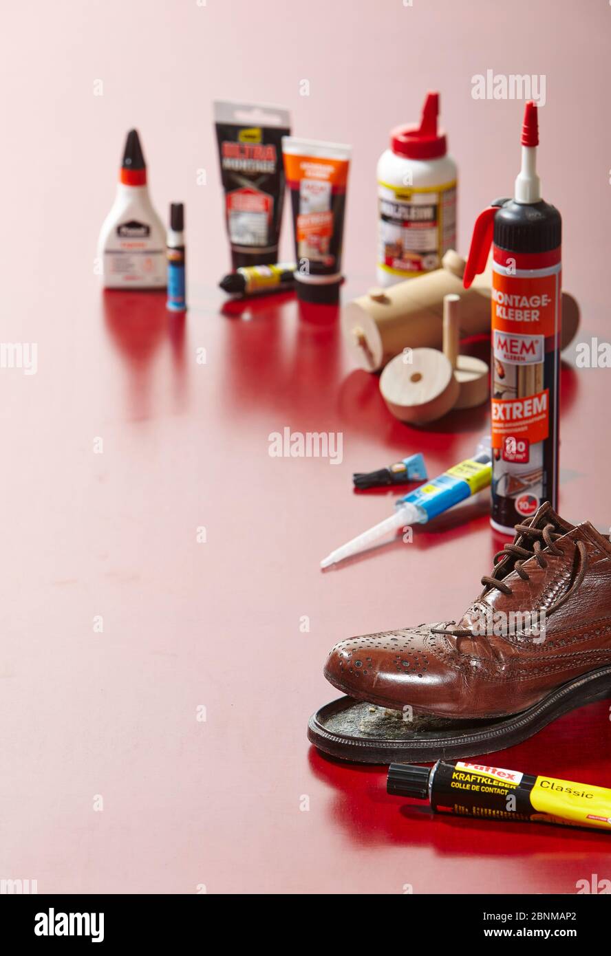 Still life studio photography on the subject of gluing. Various types of glue on a red plexiglass plate in backlight arranged with two decorative objects to be glued: Repair of a leather shoe and a wooden toy variant 01 Stock Photo