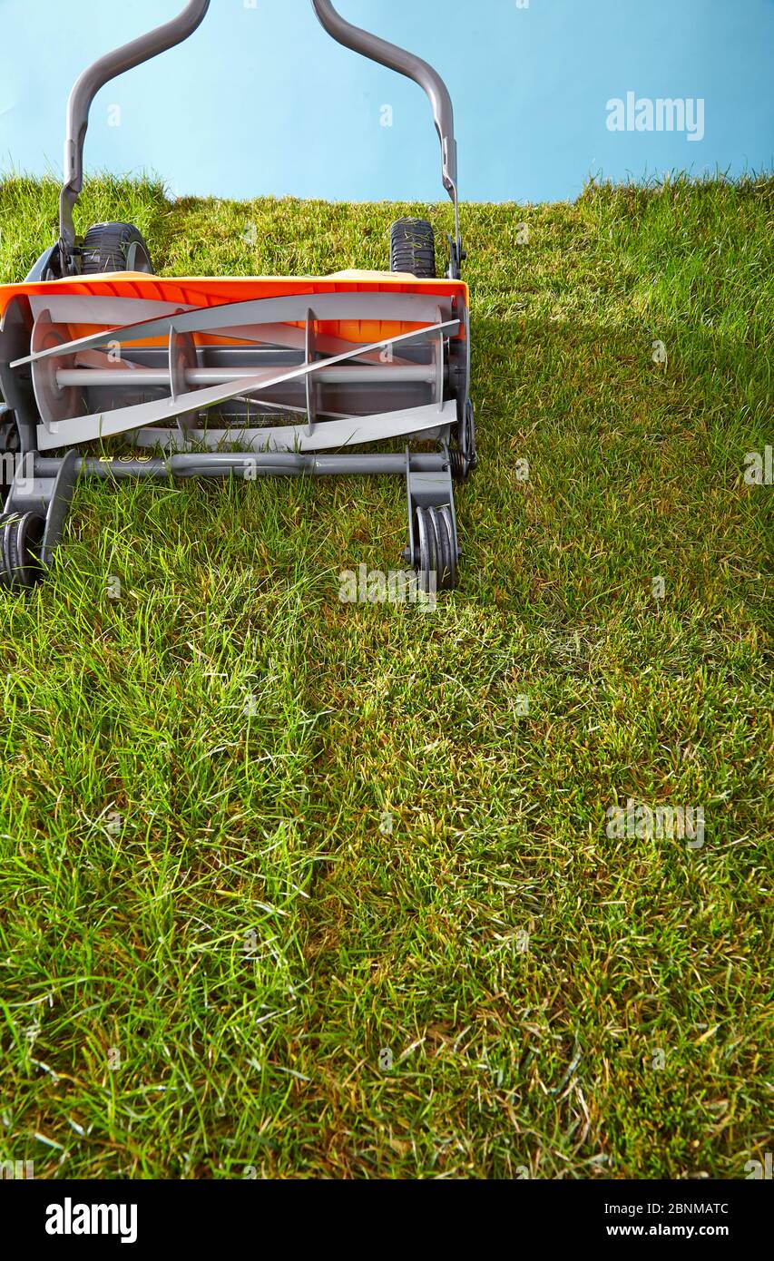Mowing the lawn by hand. Symbolic photo, spindle mower on lawn against light blue, sky Stock Photo