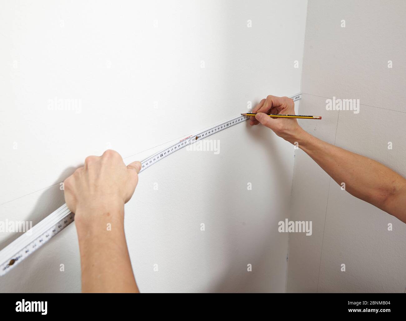 DIY wall design 01, step-by-step do-it-yourself production, vertical colored stripes in the lower wall area, step 01 measure and mark with pencil and ruler on the white painted wall Stock Photo