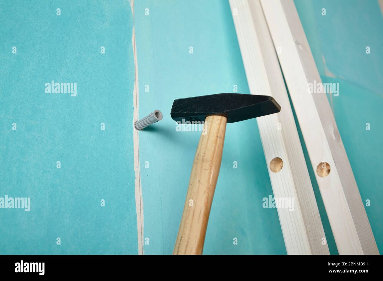 DIY wall design 02, step-by-step do-it-yourself production, various turquoise colored areas separated by white wooden strips, Step 11: hammer in a dowel into the hole in the wall to attach the strips Stock Photo