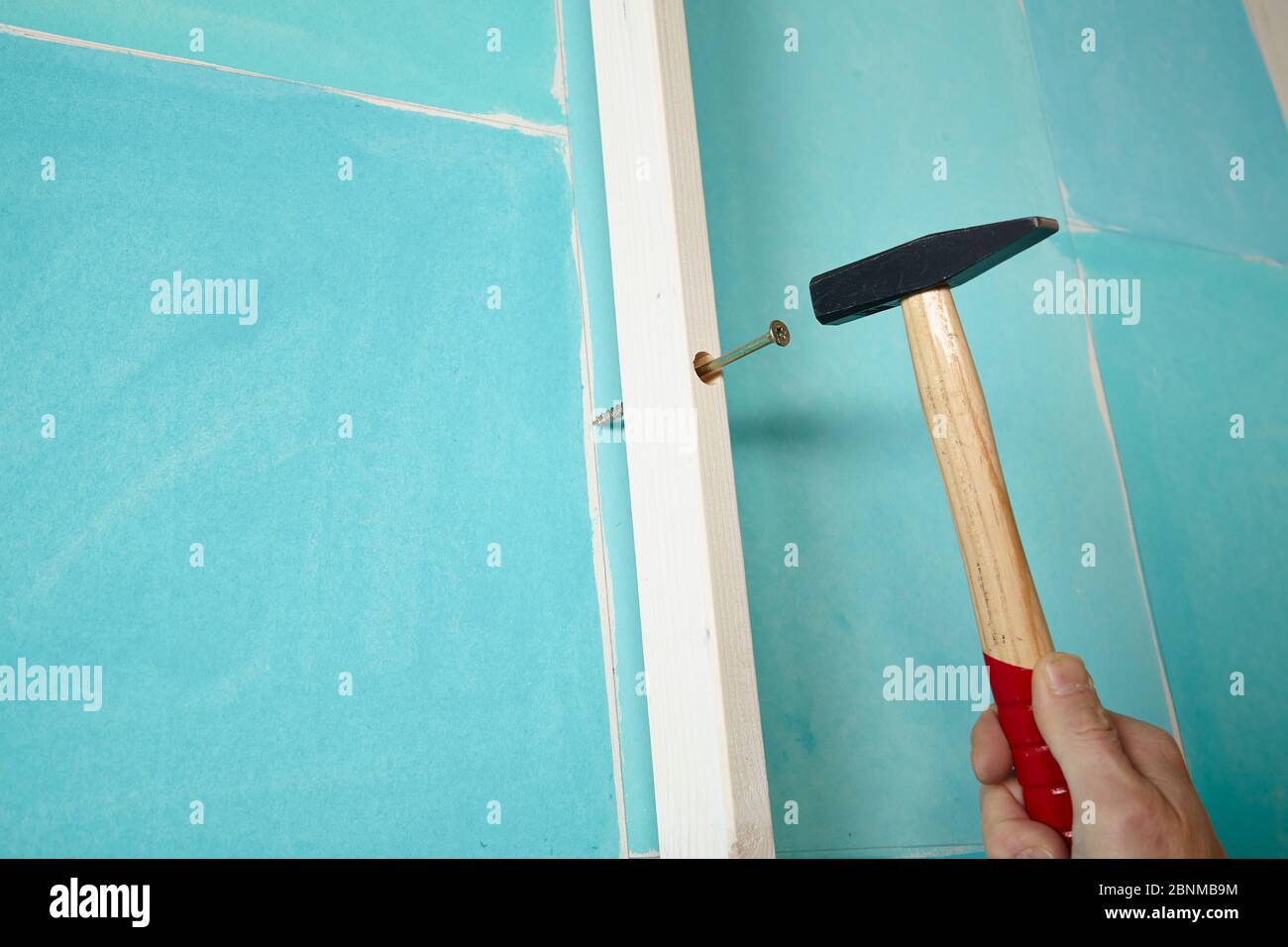 DIY wall design 02, step-by-step do-it-yourself production, various turquoise colored areas separated by white wooden strips, Step 09: Mark the drilling points in the wall for attachment to the strips, strike with a hammer on the half-screwed screw Stock Photo