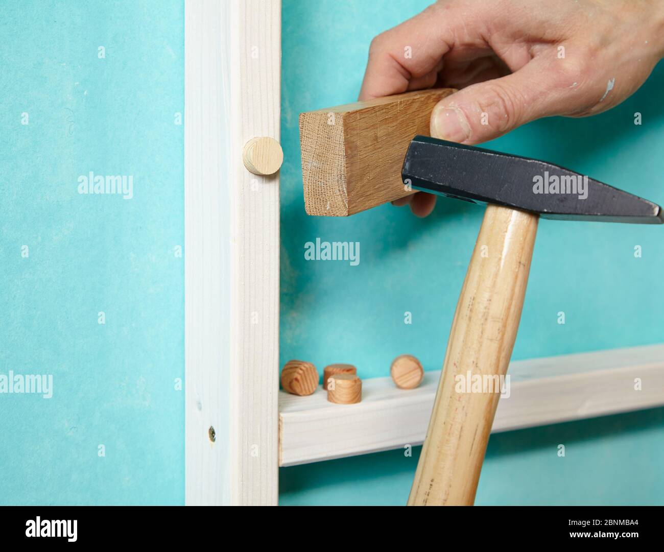 DIY wall design 02, step-by-step do-it-yourself production, various turquoise colored areas separated by white wooden strips, step 14: covering the screw holes with wooden cones, driving in with a wooden block and hammer Stock Photo
