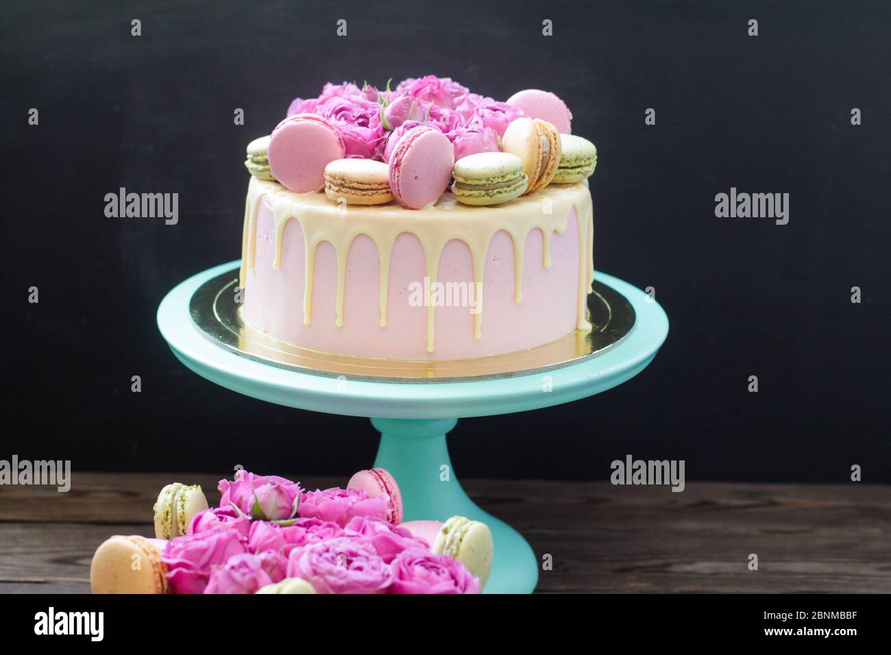 Modern pink cake with melted chocolate, fresh roses and macaroons ...