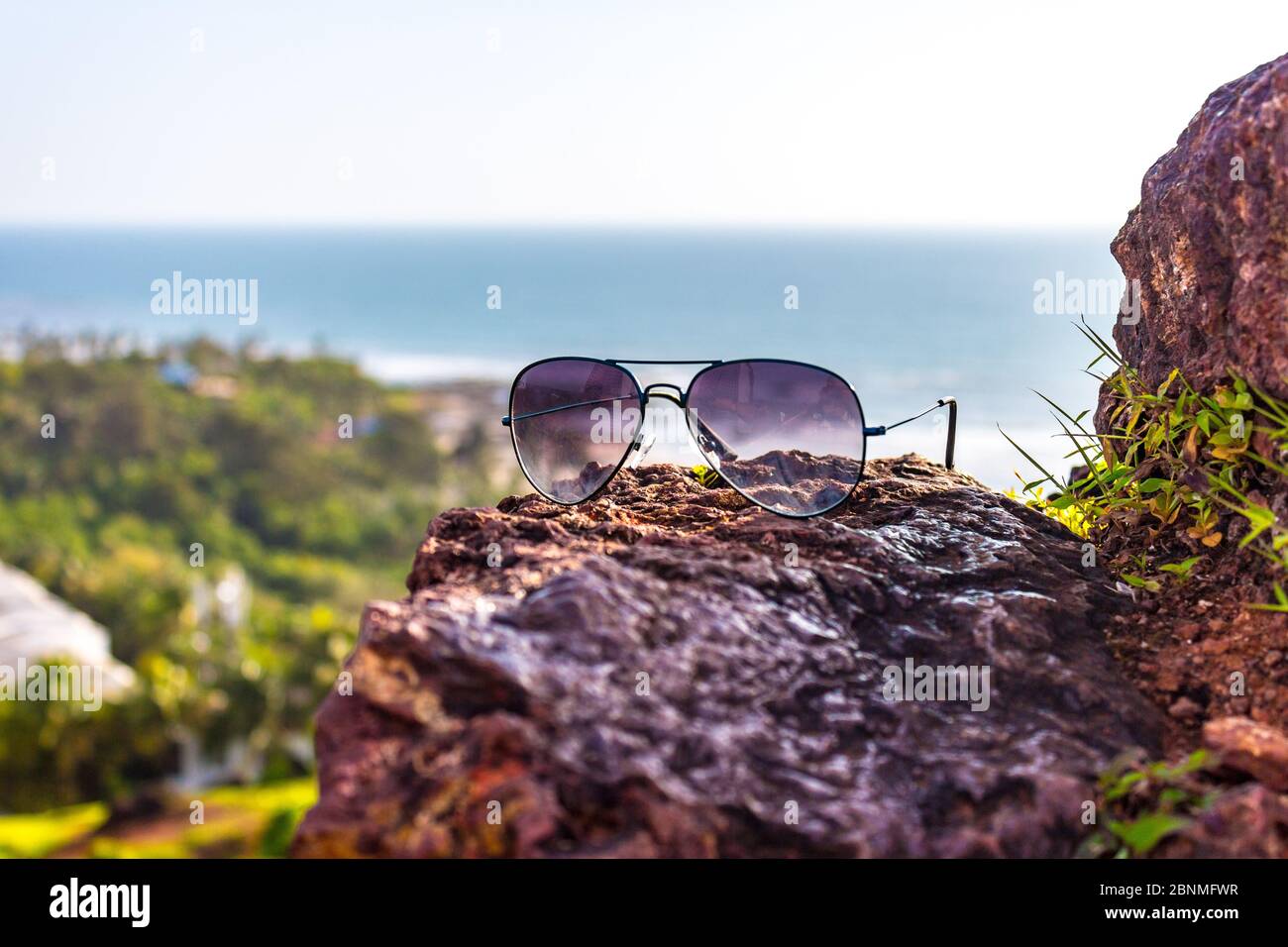 Aviator sunglasses in the focus with Vagator beach of North Goa, Goa, India in the background. Aerial view of Vagator beach from top of Chapora Fort Stock Photo