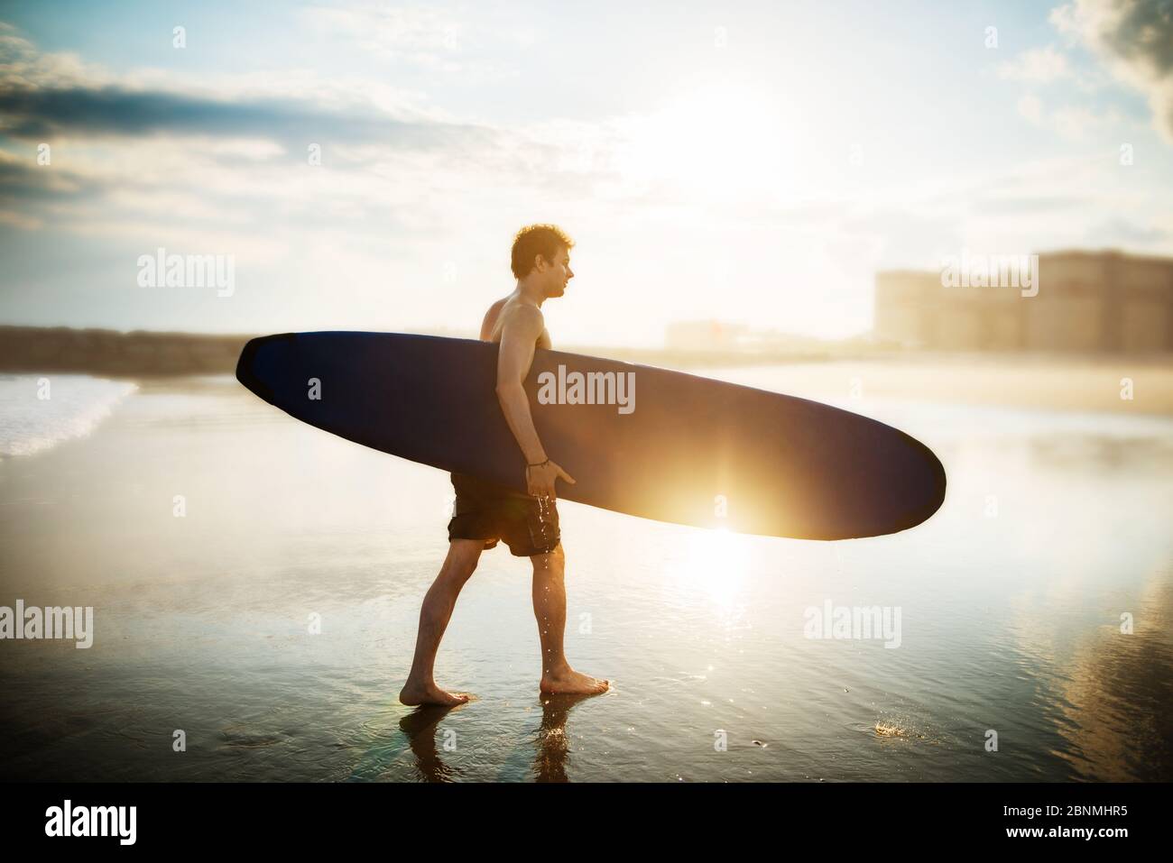 Young man walking on the beach with a surf board Stock Photo