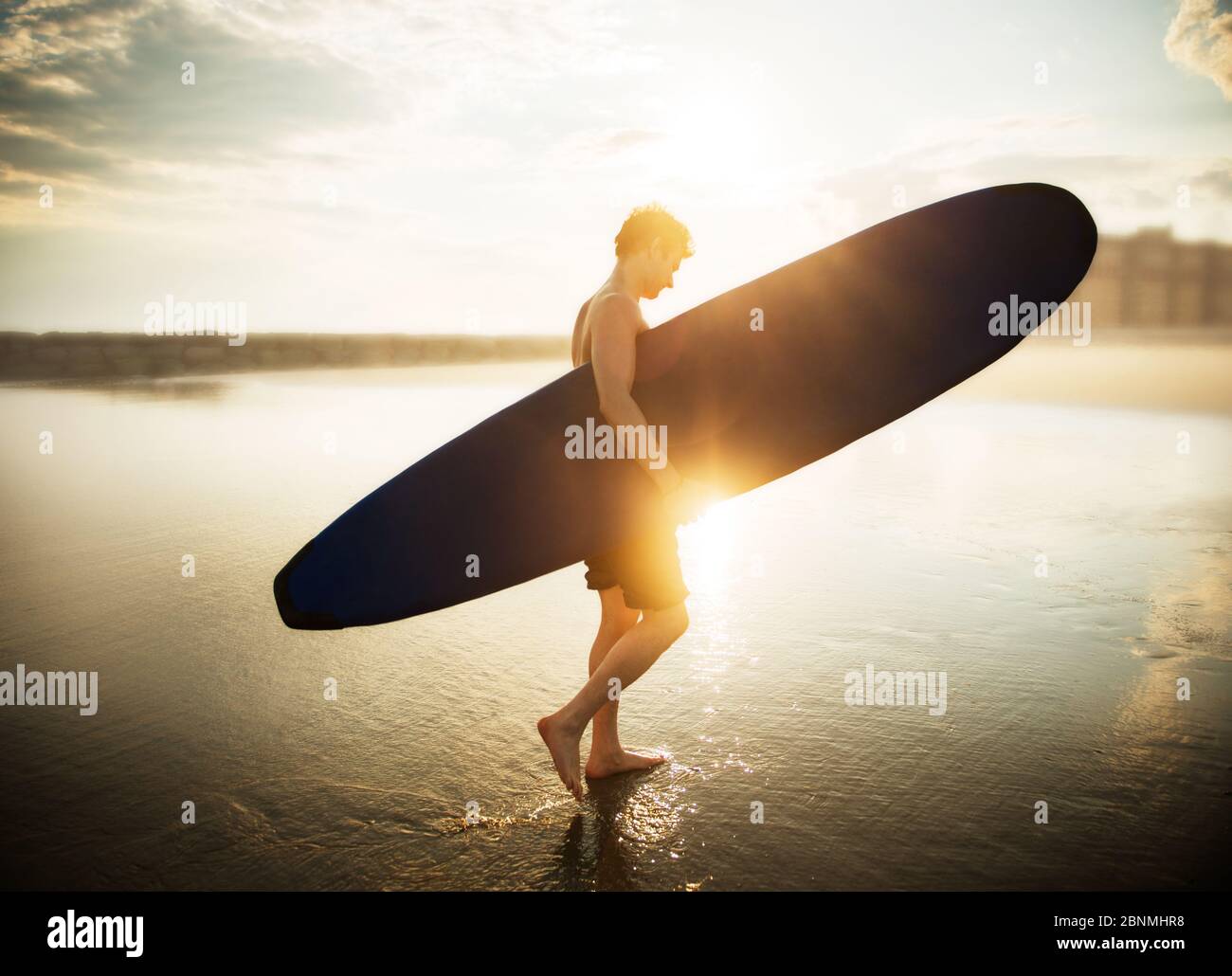 Young man walking on the beach with a surf board Stock Photo