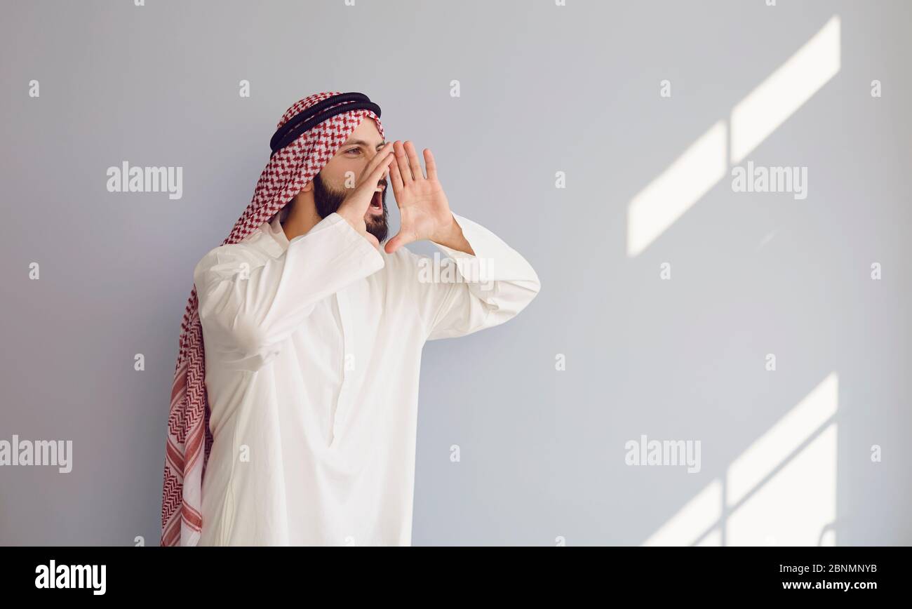 Arab man screaming calls invites informs presents on a gray background ...