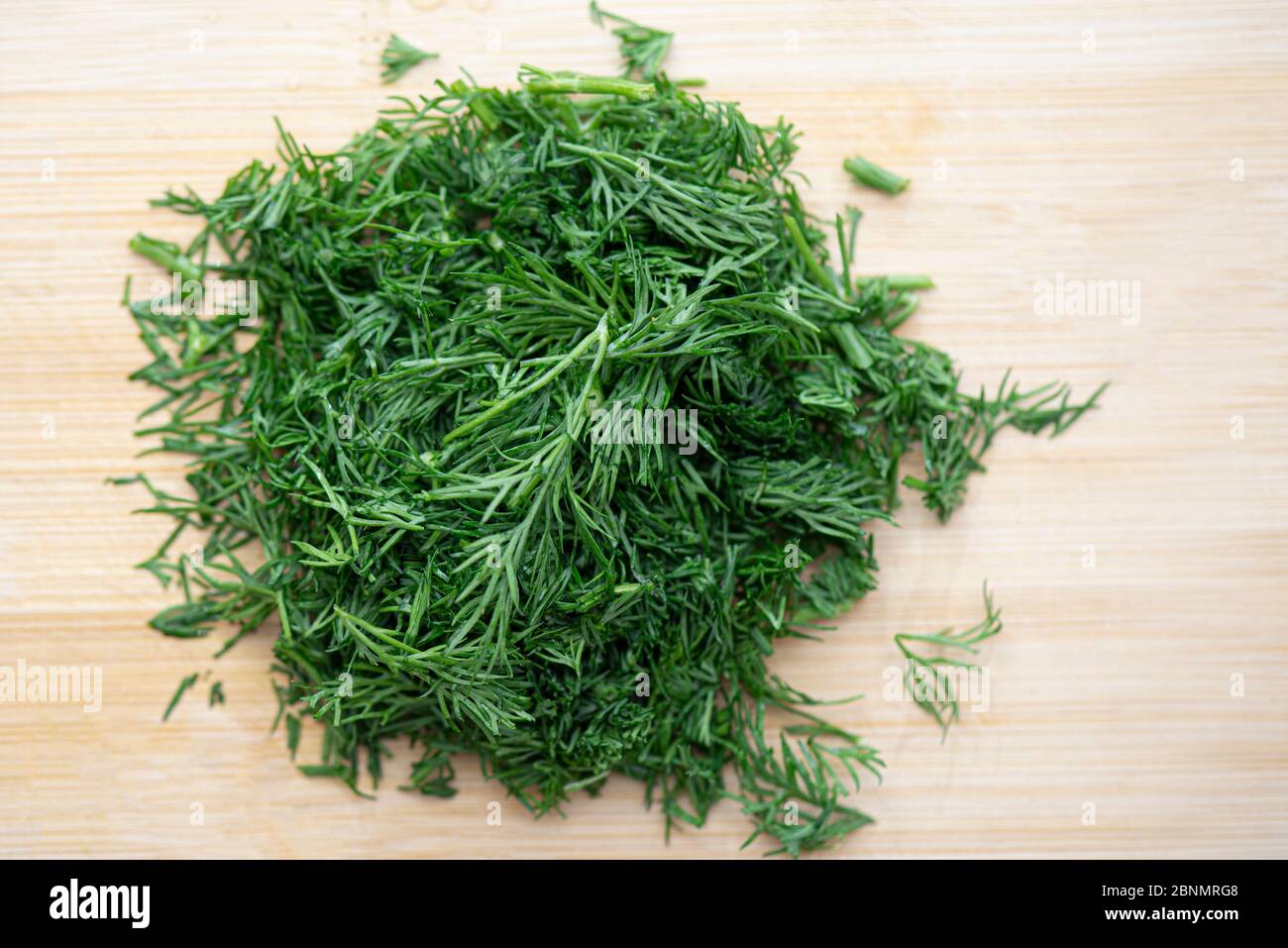 Closeup top view of chopped fresh green dill, cut dill on wooden board