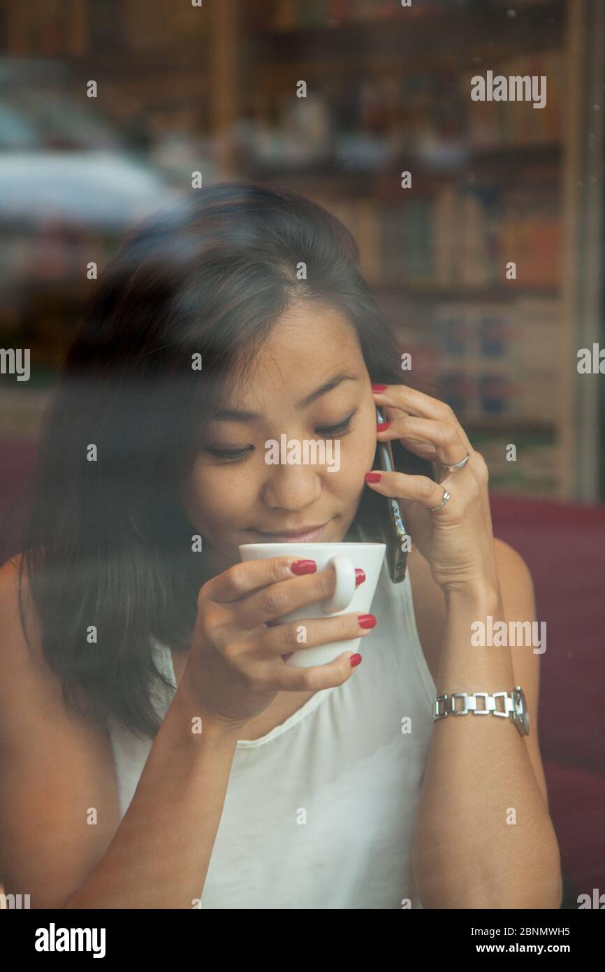 Beautiful Asian young girl sitting in a cafe by the window, drinking ...