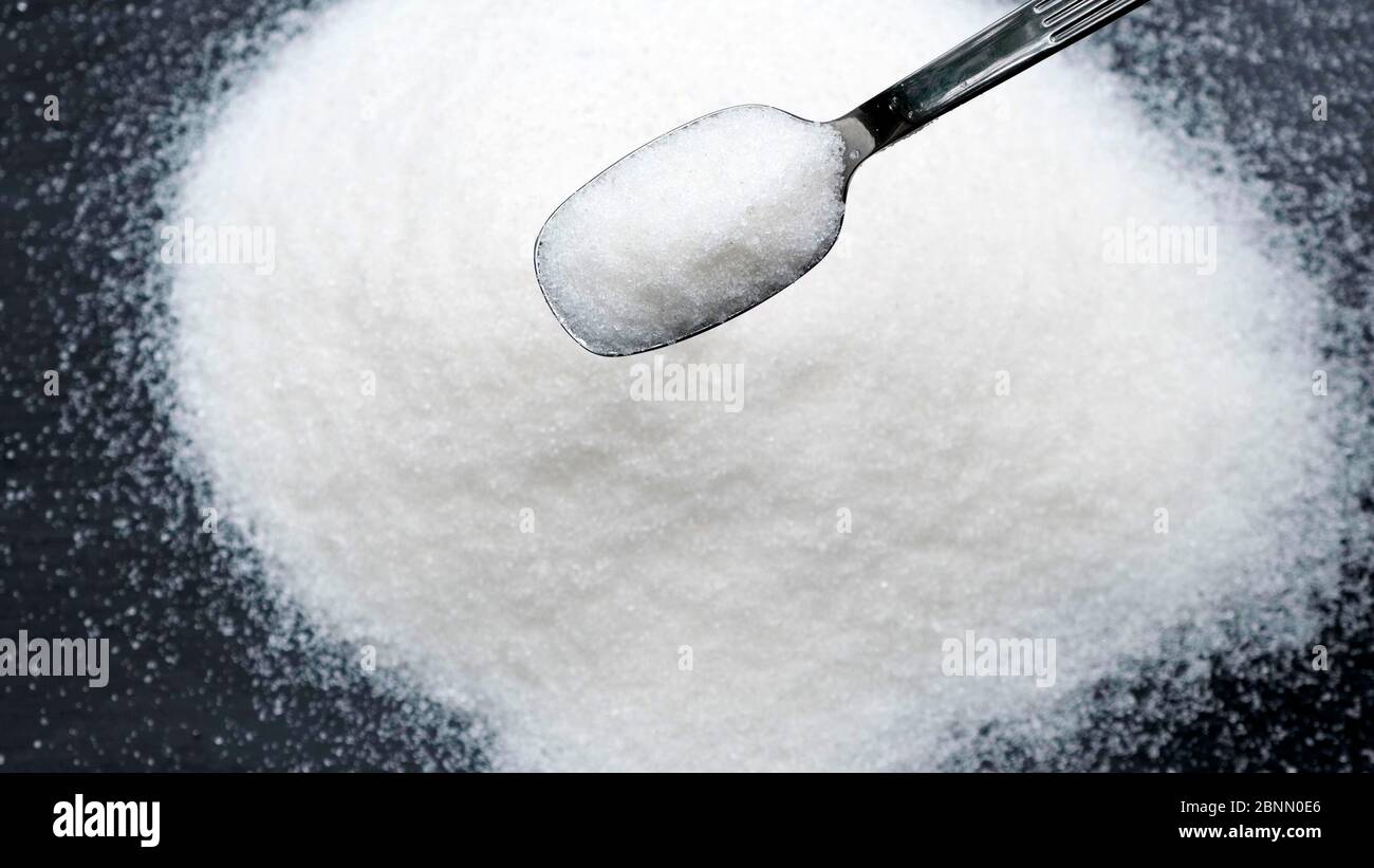 Sugar falling from spoon on black background. Stock Photo