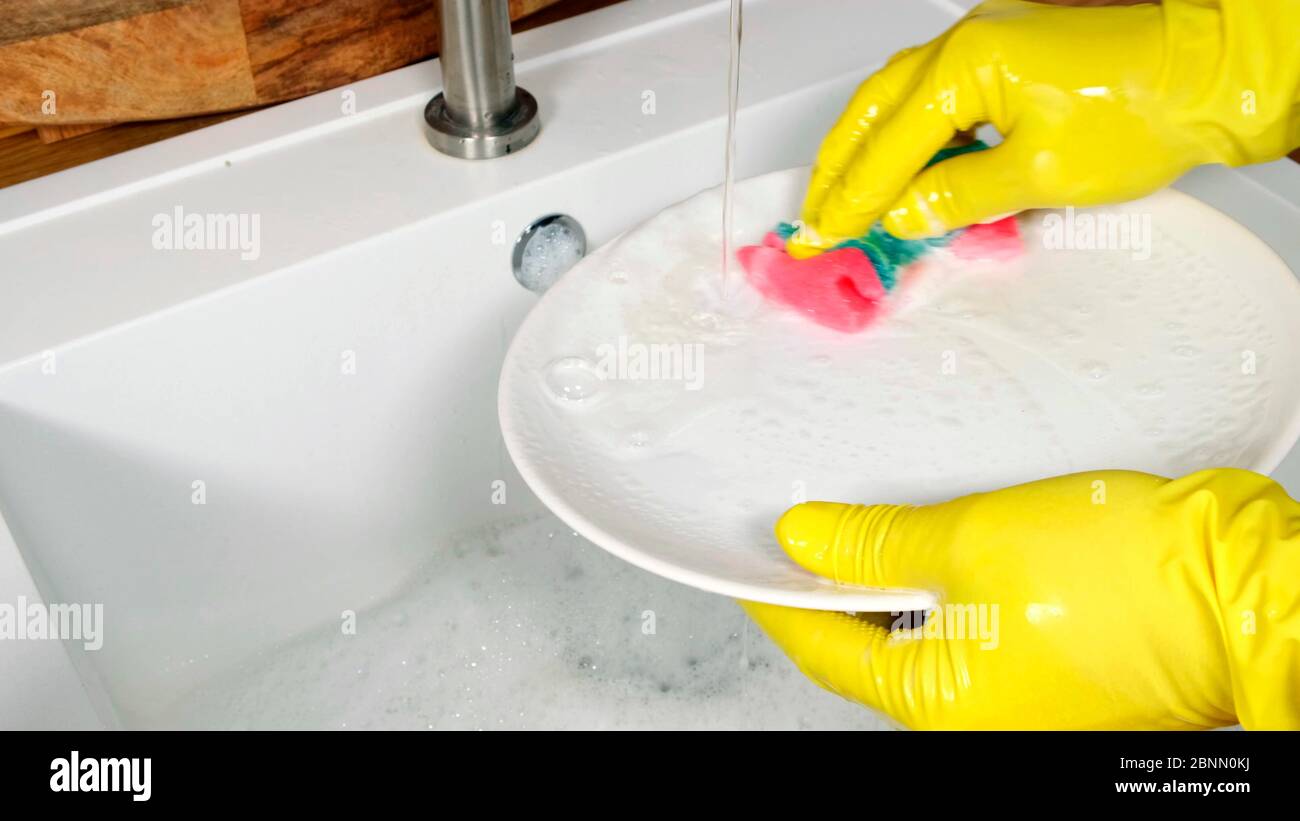 Female hands wearing yellow rubber gloves washing white plate in