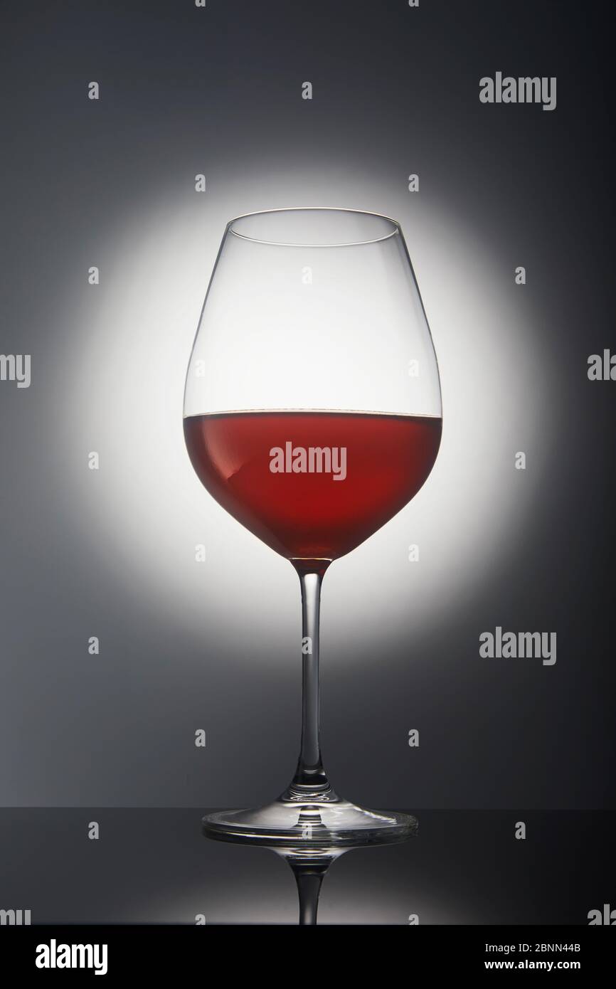 Glass with red wine on a gray background with backlight and reflection. Stock Photo