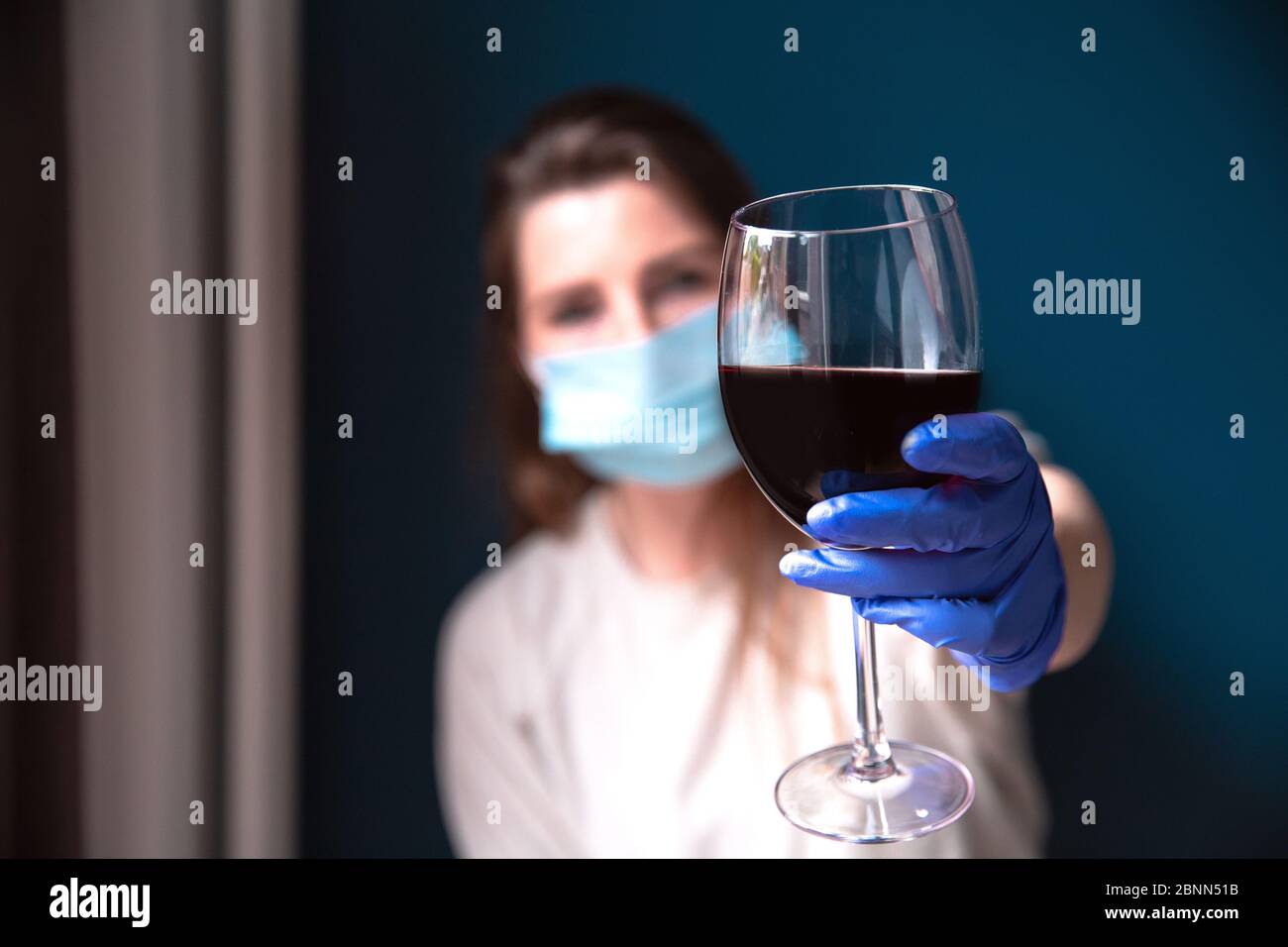 Woman wearing protective mask and blue gloves in her home and drinking red wine, self isolated for Coronavirus Covid-19, sad and lonely Stock Photo
