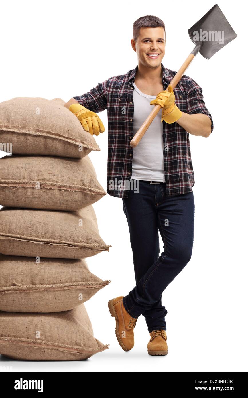 Young farmer standing with a spade and leaning on a pile of sacs isolated on white background Stock Photo