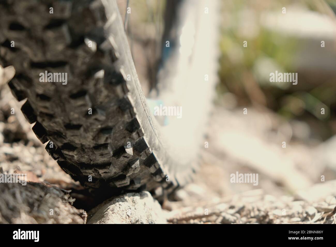 close up shot bicycle wheel with rim rolling over the rock on gravel. Blurry background daylight. Stock Photo
