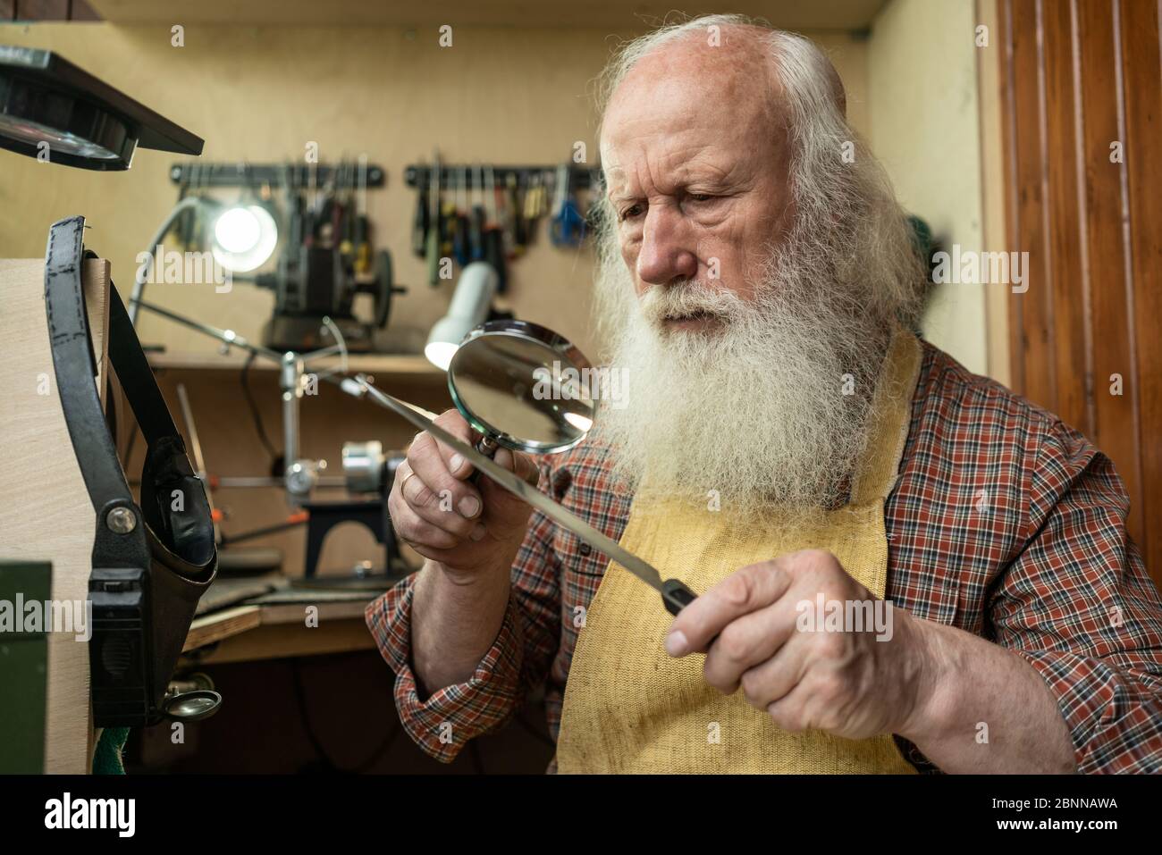 A man looks through a magnifying glass on the cutting edge of the knife to check its sharpening Stock Photo