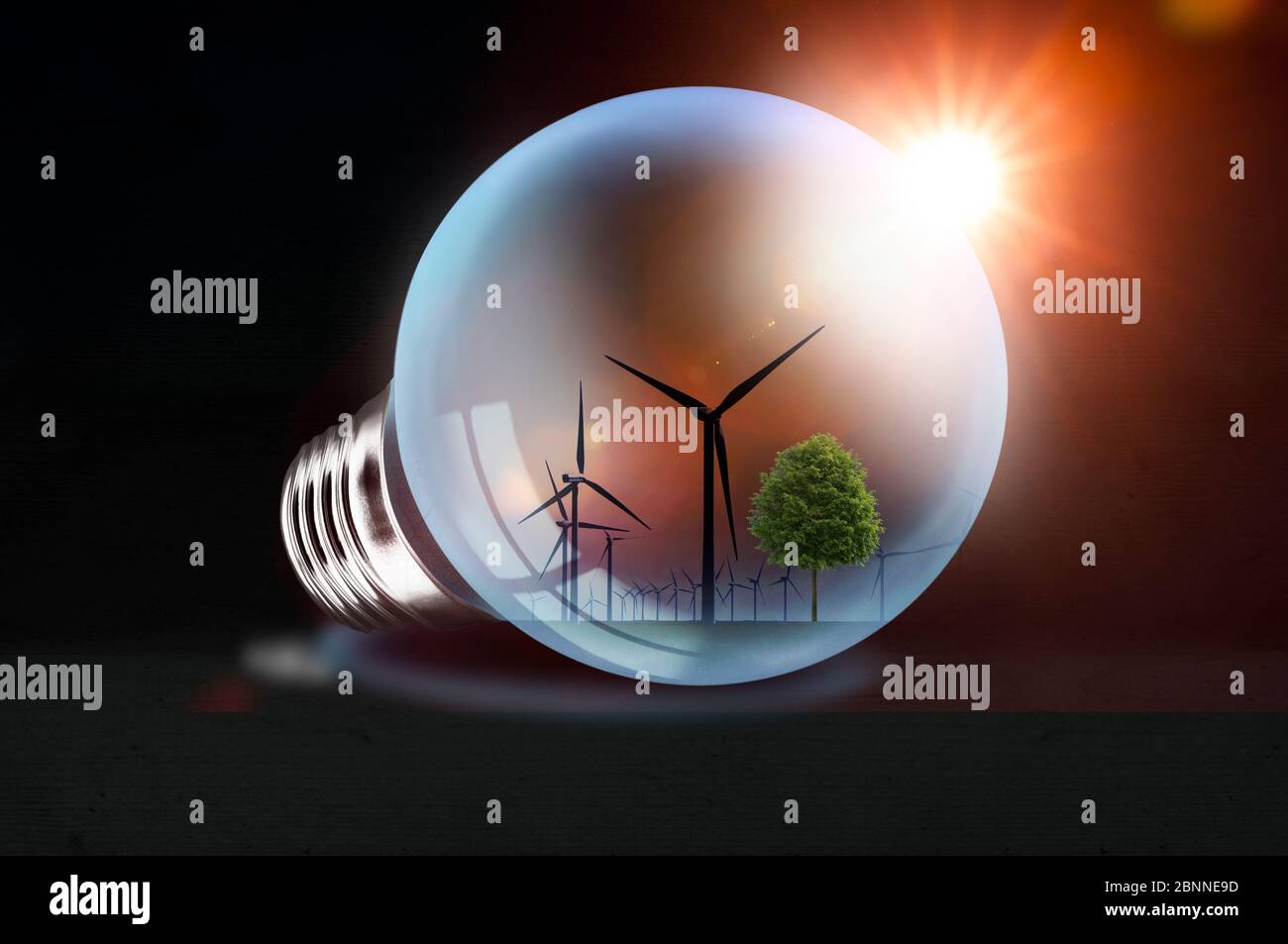 Glowing light bulb on dark background with wind farm reflection - concept Stock Photo