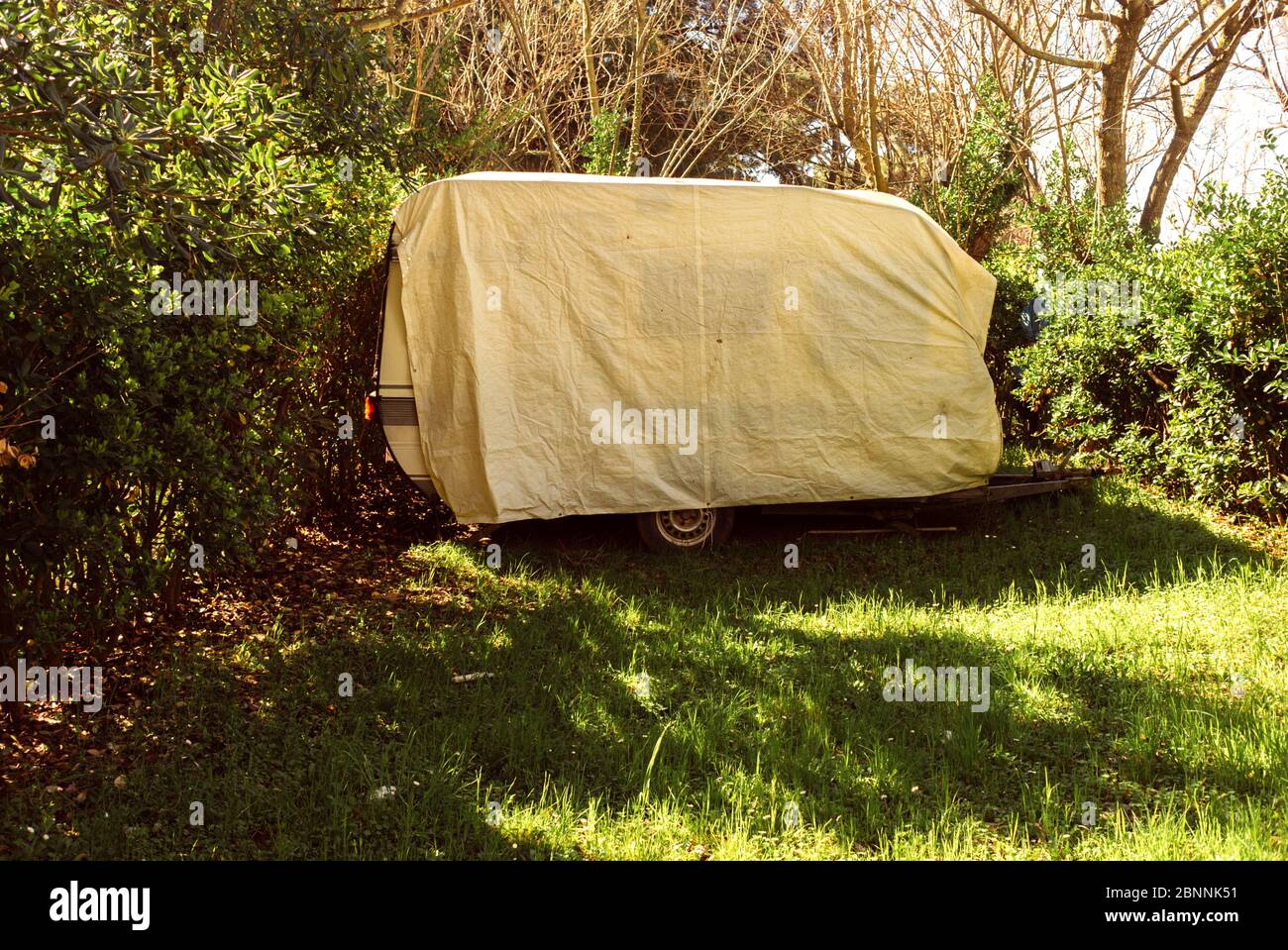 Old caravan trailer packed with tarp in a camp site. Thassos, Greece Stock Photo