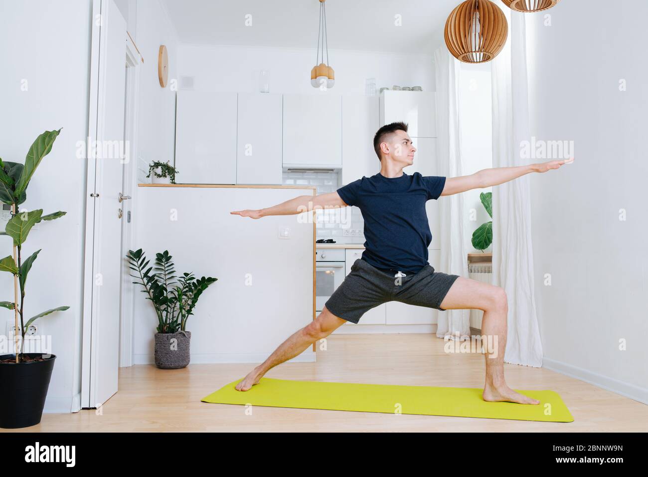 Tall man doing yoga on a mat at home, warrior form variation Stock Photo -  Alamy
