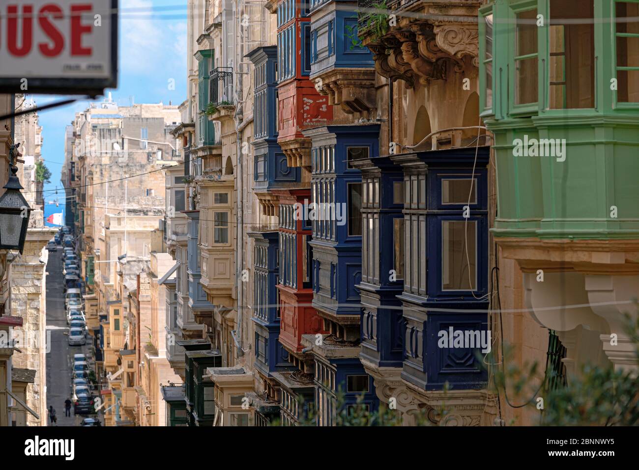 View from above into a long narrow alley of Valletta with the typical facade architecture, at the end blue Mediterranean Stock Photo