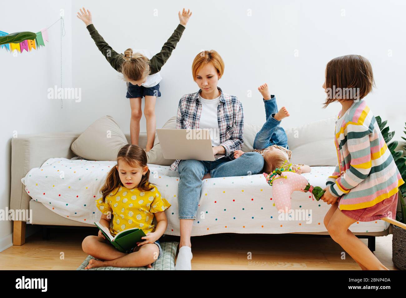 Freelancer woman working on a laptop next to her loud kids Stock Photo