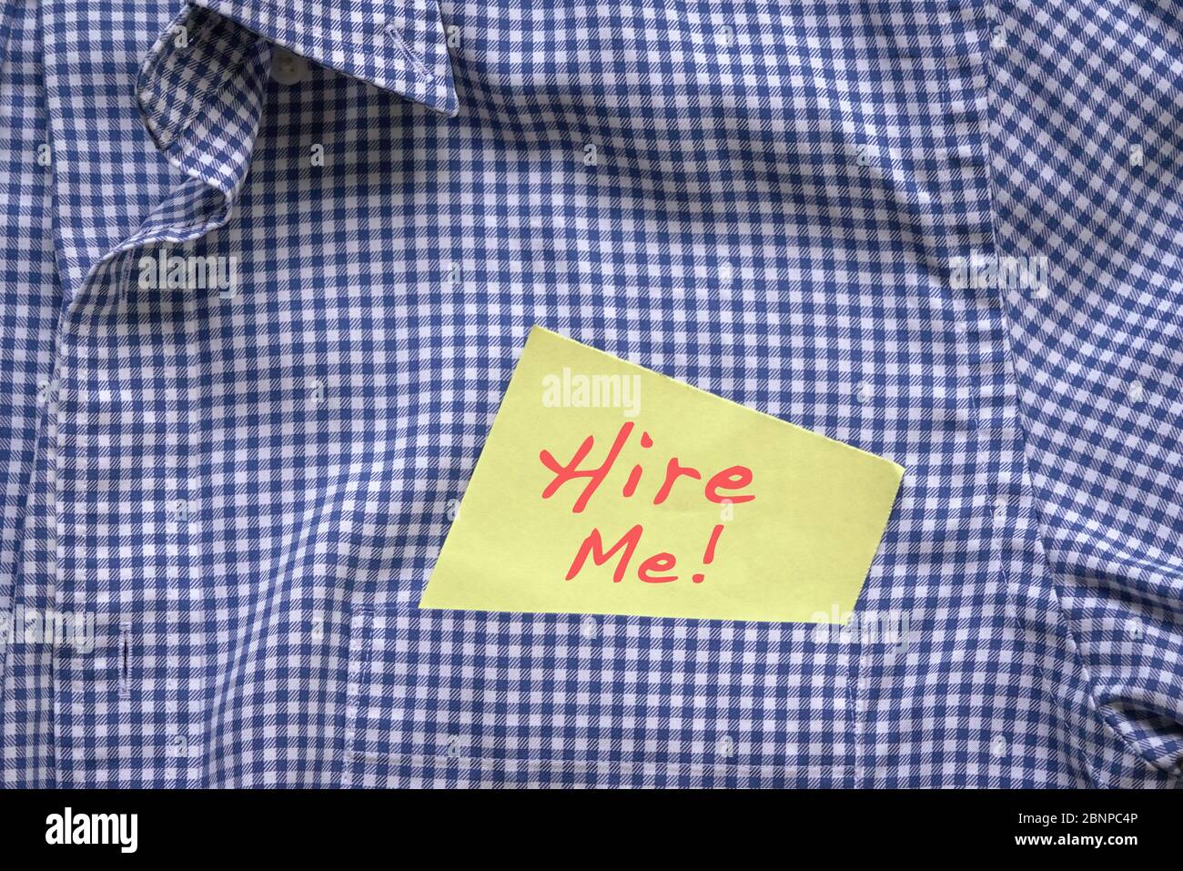 Hire me, words in red on a yellow paper stuck out from blue shirt pocket. Employment concept. Stock Photo
