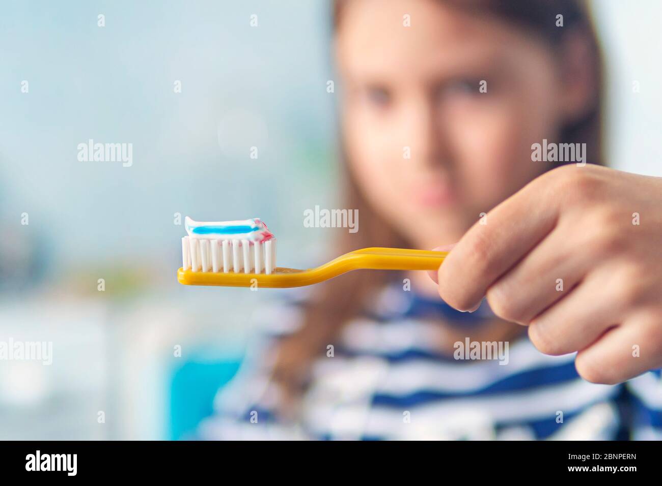 Little girl brushing teeth. Close-up photo. striped toothpaste on a toothbrush on a blurred background of a child. Stock Photo