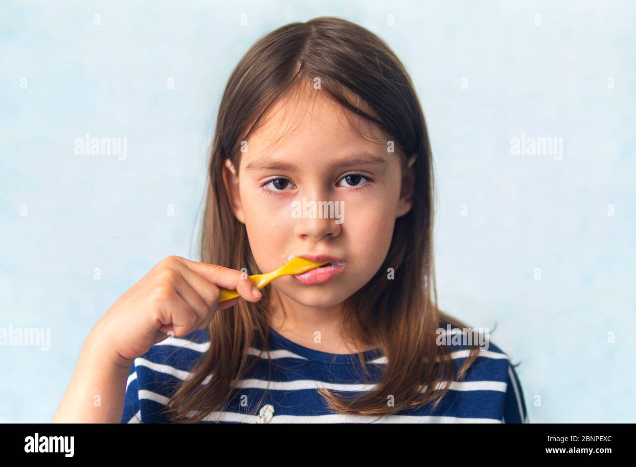 Toddler smiling while brushing her teeth. blue background. A little girl of Caucasian appearance brushing her teeth with a toothbrush, Hygiene procedu Stock Photo