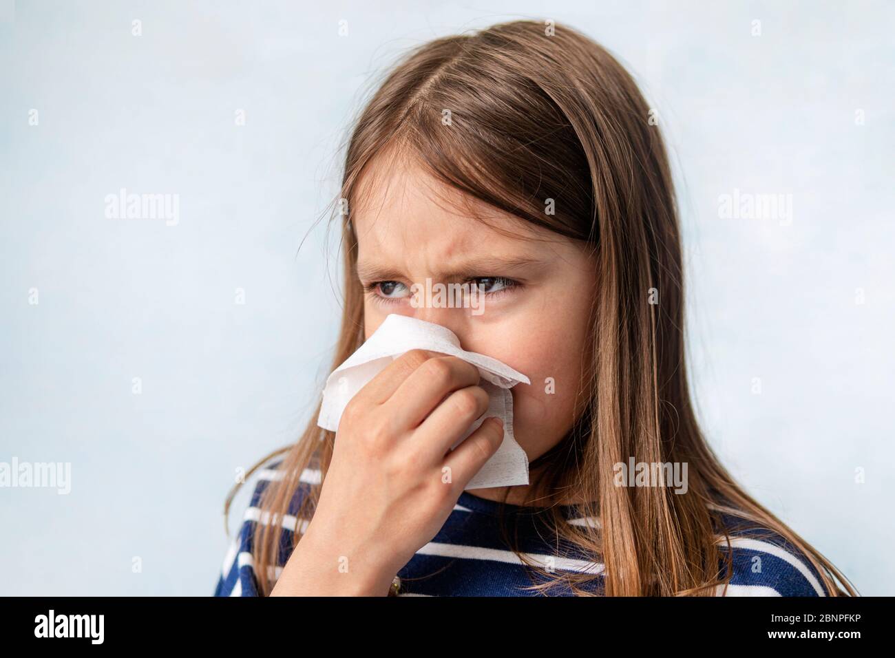 resentment and tears. The child is crying and wipes his snot with a white wet napkin. A girl sneezes into a rag on a blue background. An unhealthy chi Stock Photo