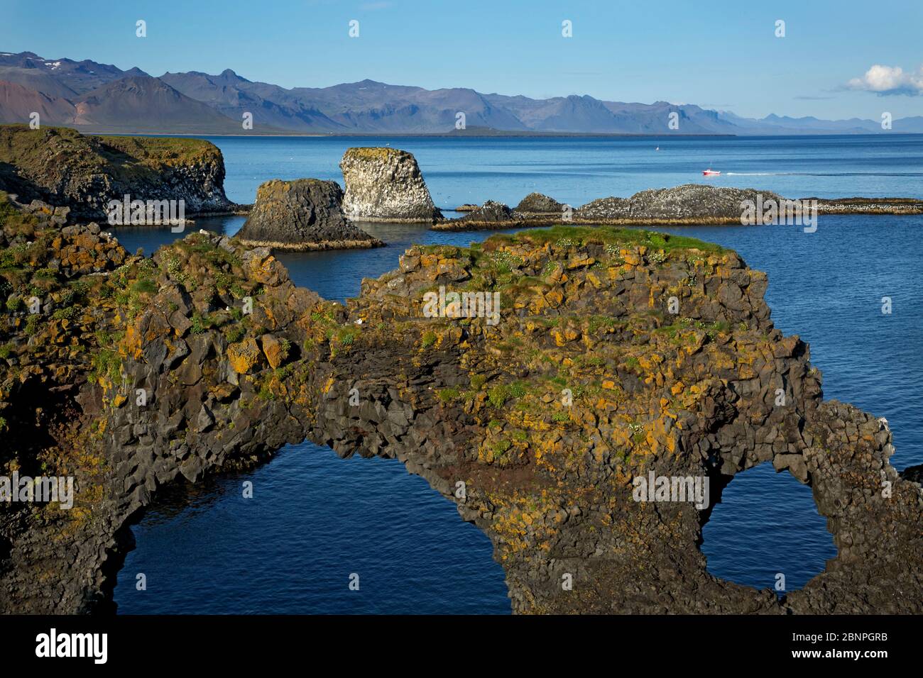 Basalt cliffs on the coast at Arnarstapi. View over the rock arch 'Gatklettur' and the basalt cone 'Musargja' to the mountain range of Snaefellsnes. Stock Photo