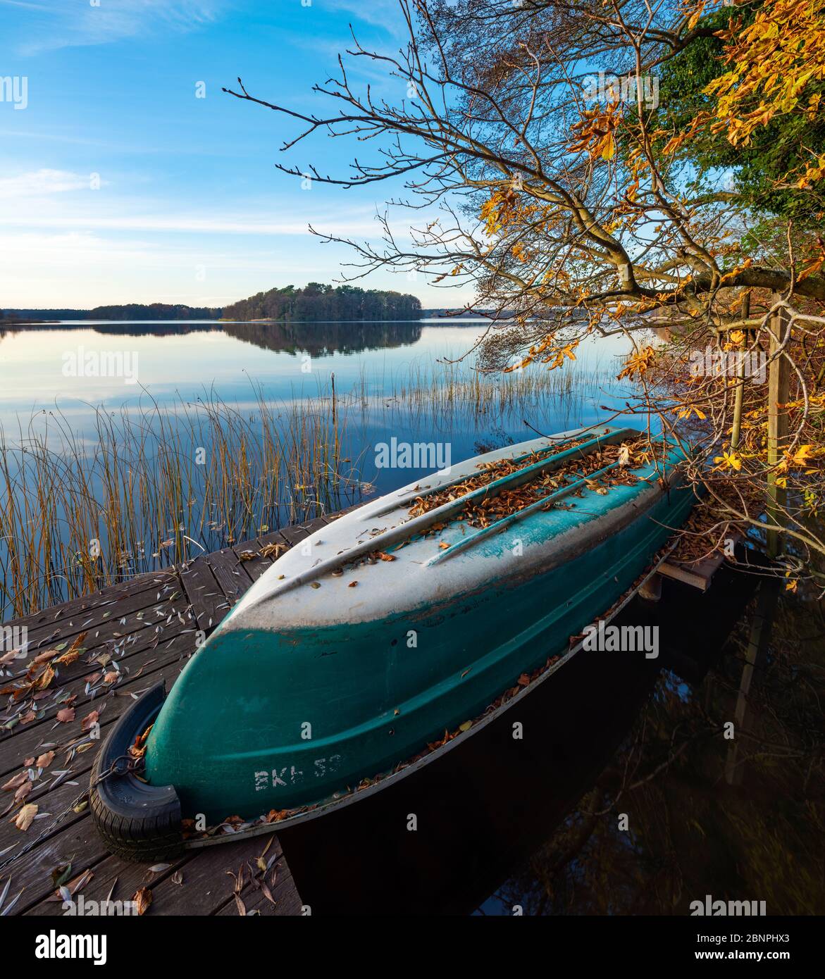 Germany, Brandenburg, Lychen, Quiet evening at the Great Lychensee in autumn, rowboat lies upside down on jetty, colorful foliage Stock Photo