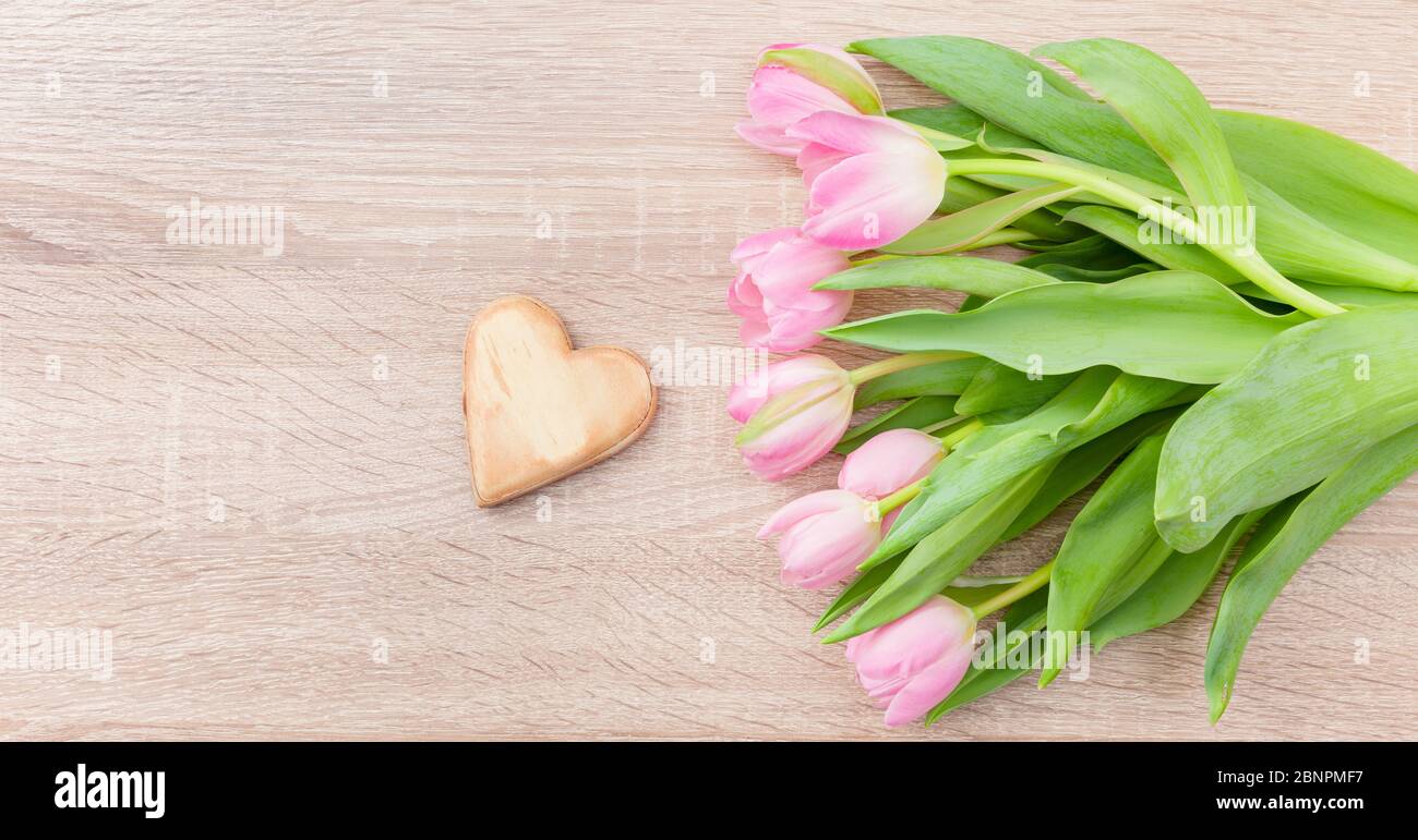 Pink red tulips on a light wooden table with wooden heart Stock Photo