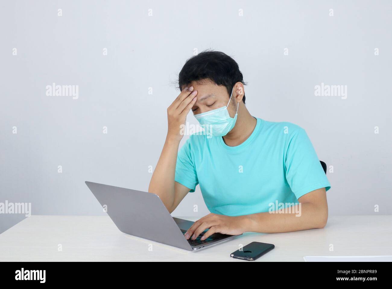 Young Asian man wearing medical mask is feeling unhealthy, tired, and confused with working in laptops on the table. Stock Photo