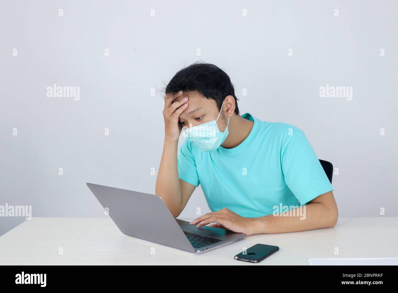 Young Asian man wearing medical mask is feeling unhealthy, tired, and confused with working in laptops on the table. Stock Photo