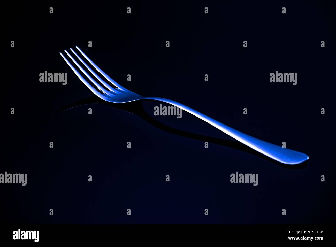 A metal fork with a blue neon reflection rests on a black glass. Advertising of the kitchen item Stock Photo
