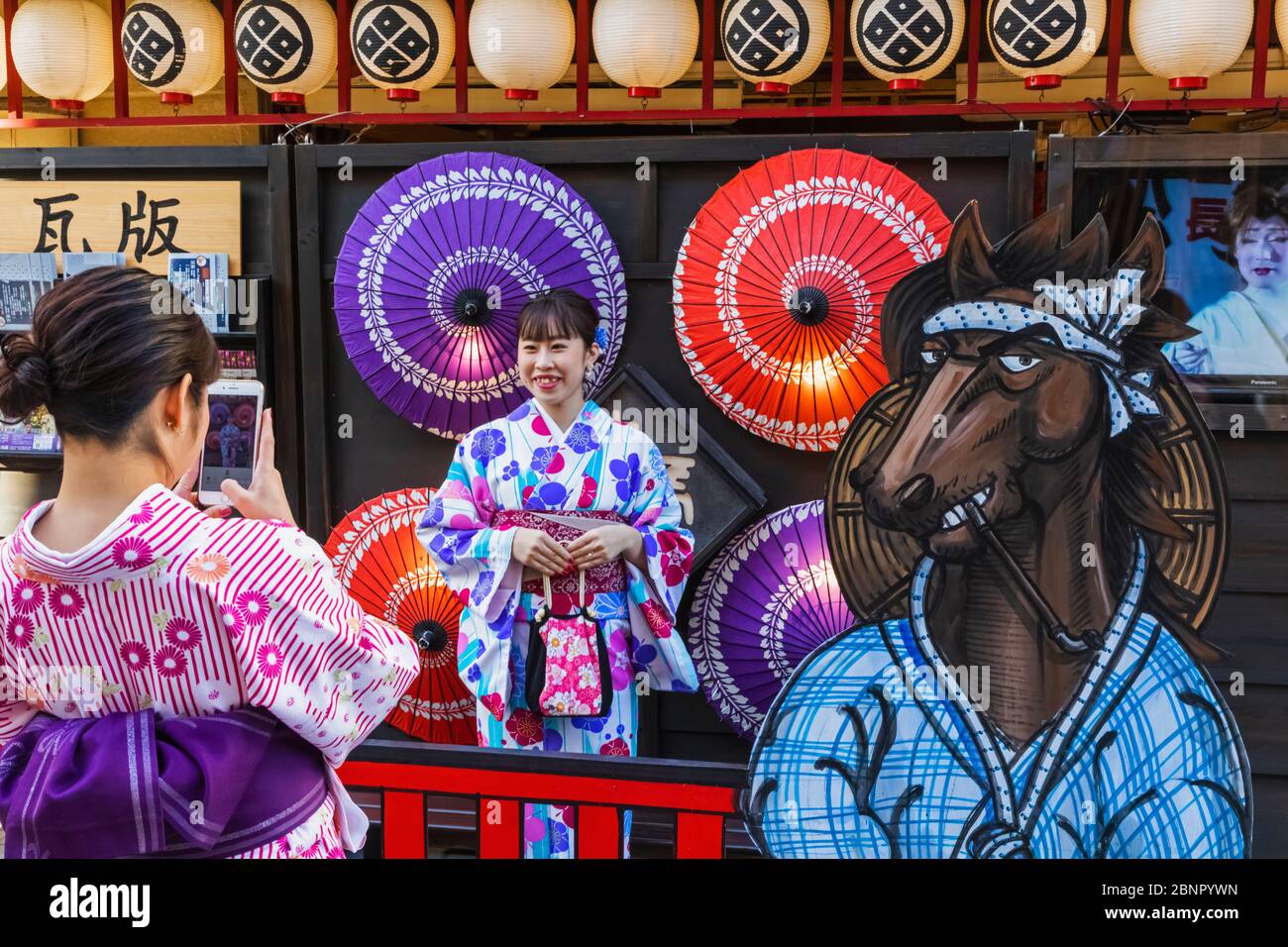 Japan, Honshu, Tokyo, Asakusa, Women in Kimono Taking Souvenir Photos in front of Colourful Paper Umbrellas Stock Photo