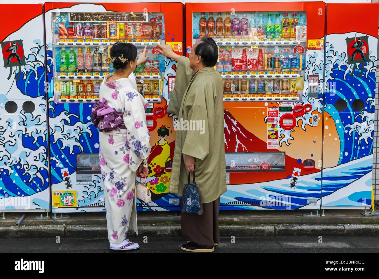 Japan, Honshu, Tokyo, Asakusa, Couple Dressed in Traditional Japanese Clothing Buying Drinks from Street Vending Machine Stock Photo