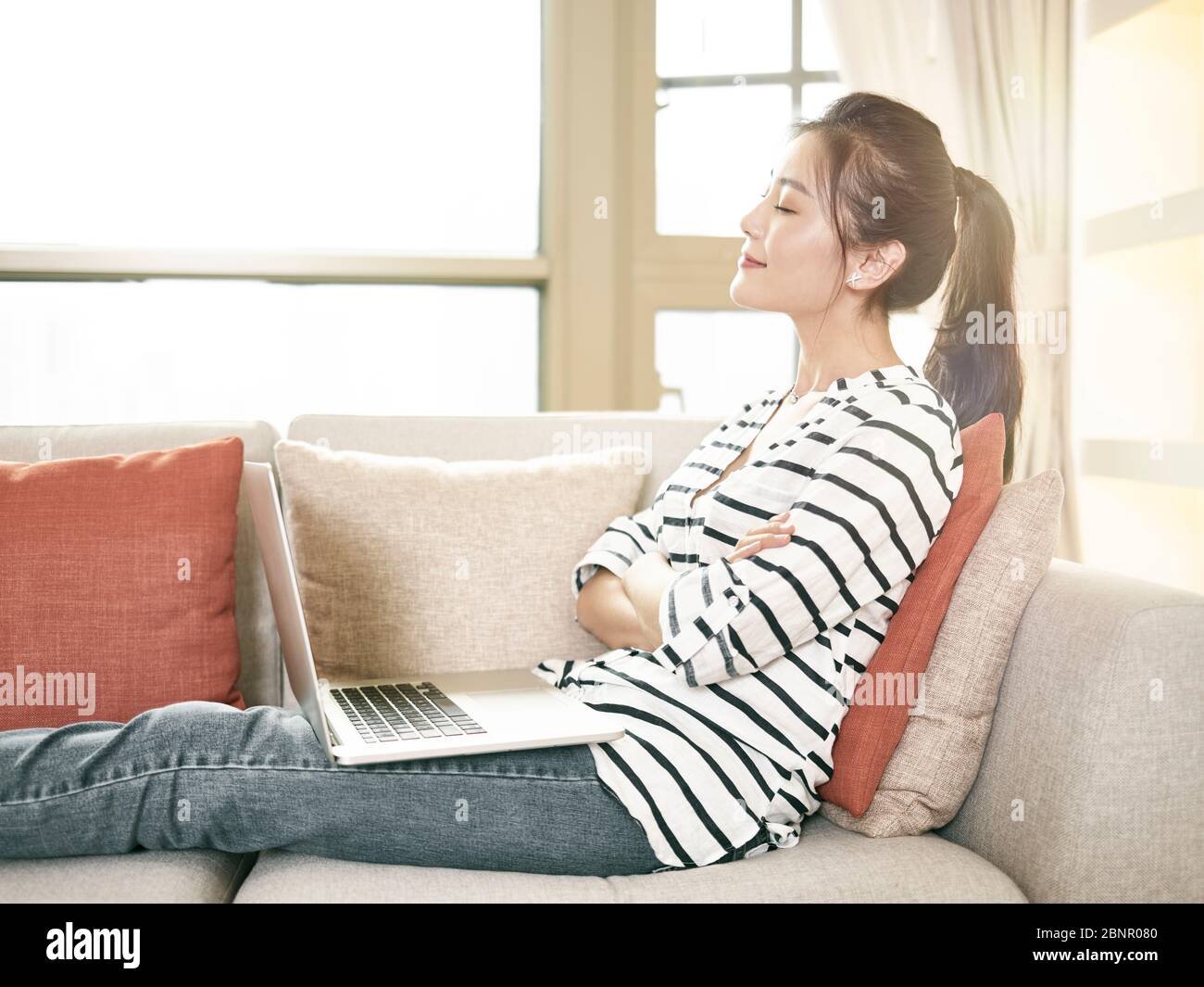 young asian woman working from home sitting on couch using laptop computer Stock Photo