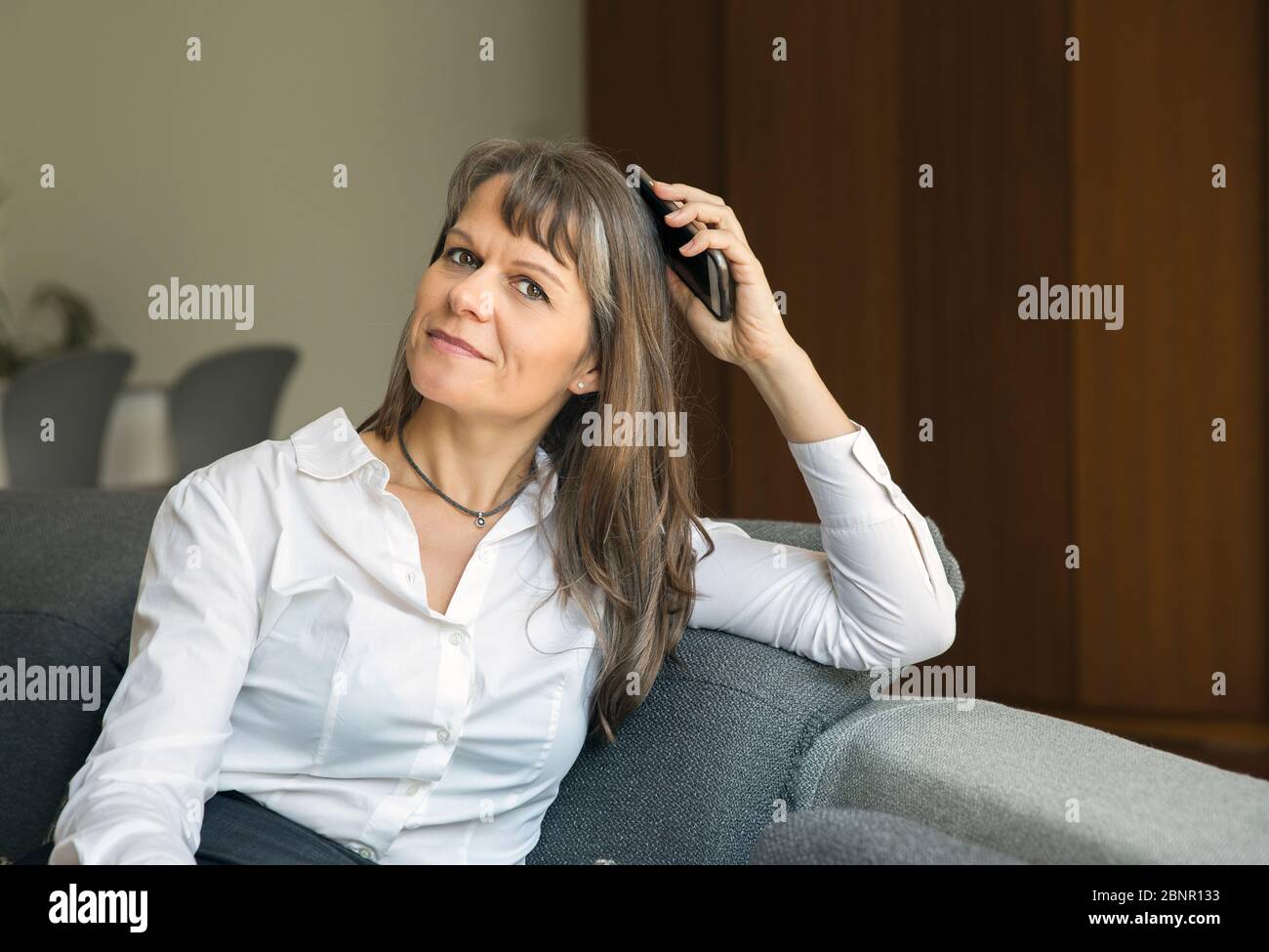 middle aged woman in formalware in her city apartment, holding a phone Stock Photo