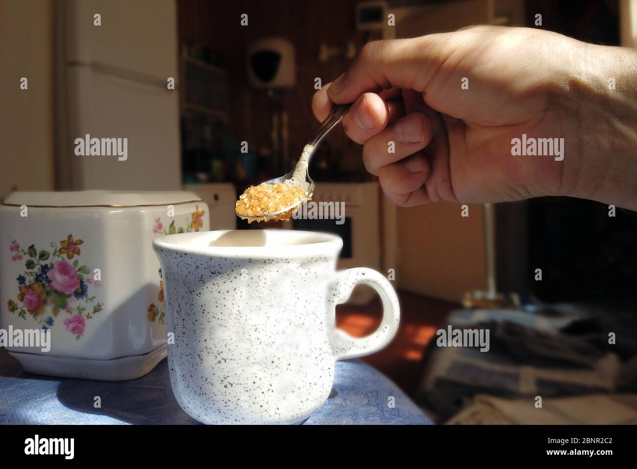 Closeup indoor shot of a hand adding sugar into a cup Stock Photo