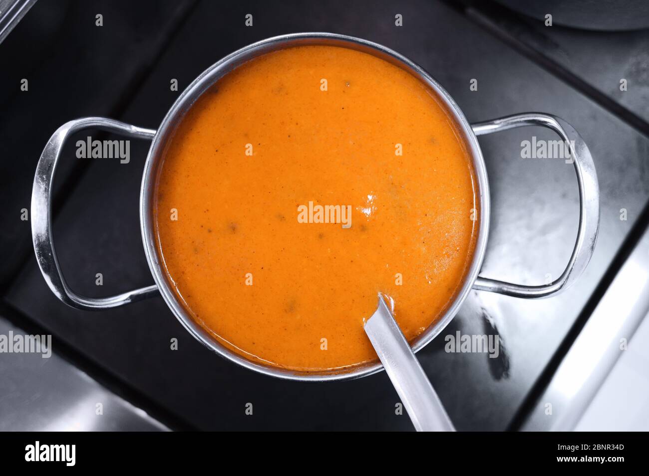 Yellow thick soup in a metal pot on the stove. Style and minimalism in the kitchen design. Stock Photo