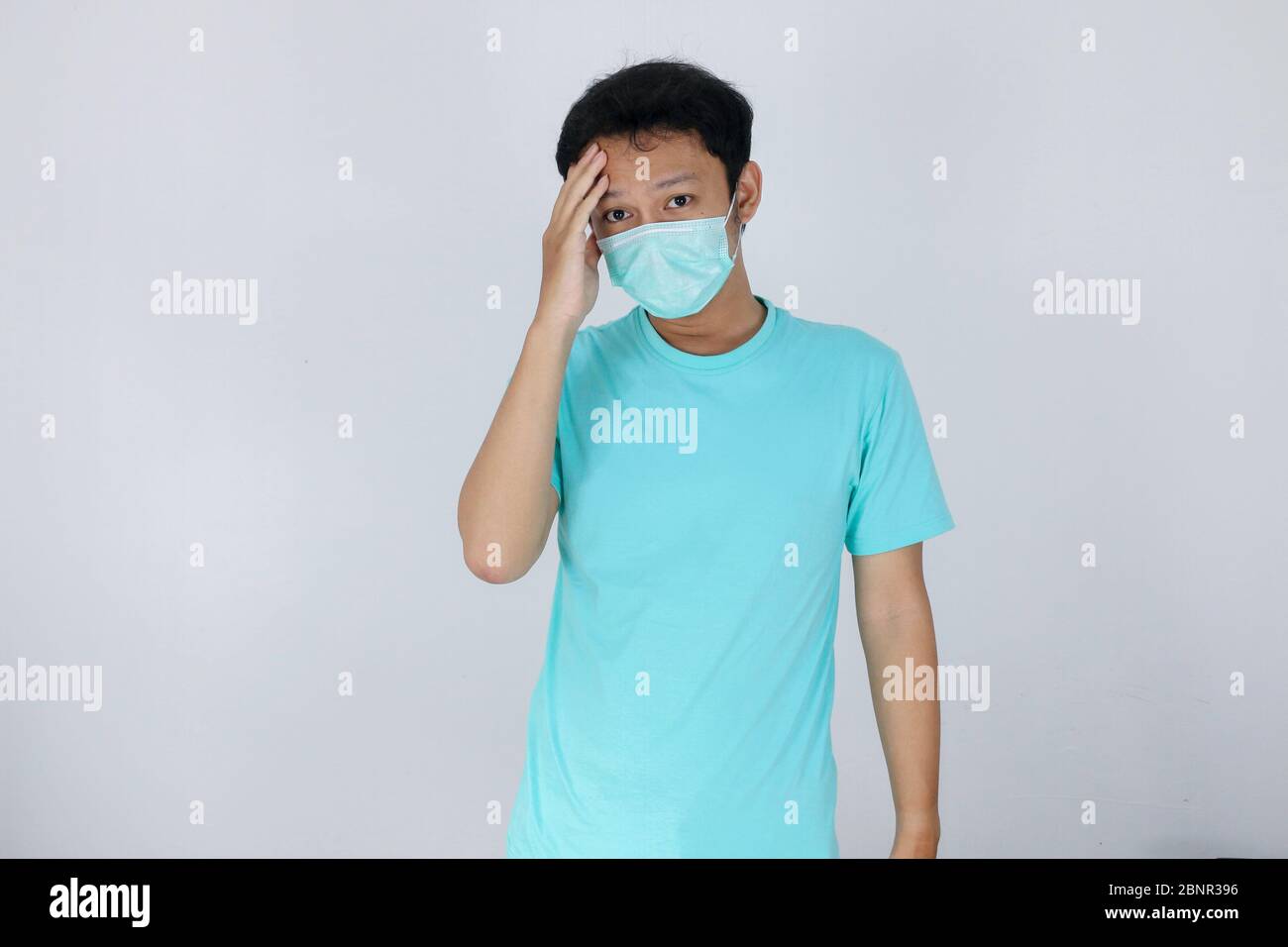 Young asian man wearing medical mask is suffering from severe headache ...