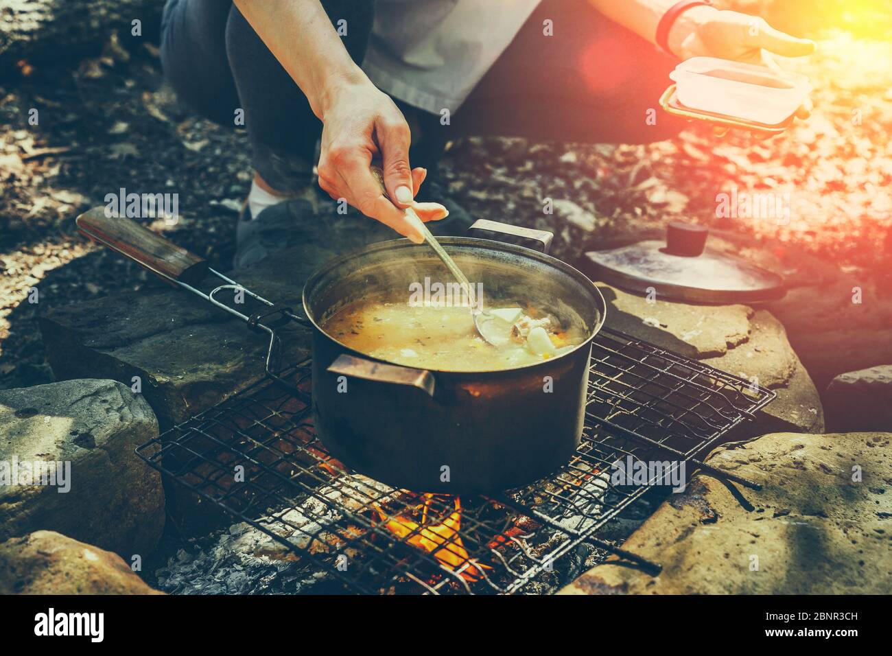 Unrecognizable woman tourist cooking on campfire in forest. Concept Tourism Camping Survival Wildlife Stock Photo