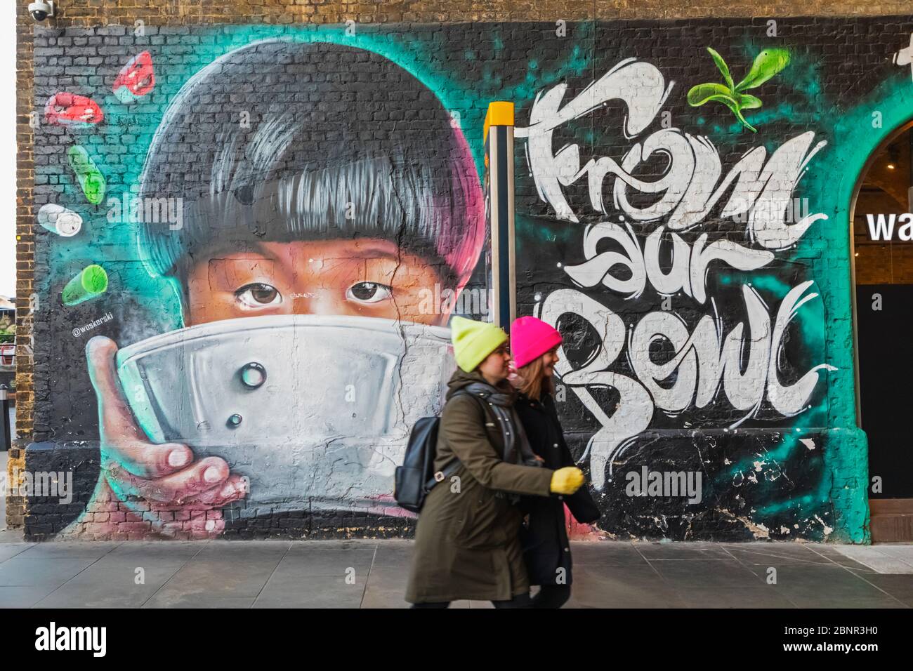 England, London, Southwark, Clink Street, Two Girls Walking Past Wall Mural Street Art depicting Asian Child Eating from Bowl Stock Photo