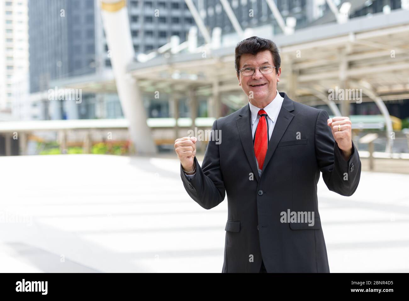 Mature happy businessman in front of modern building at Bangkok city ...