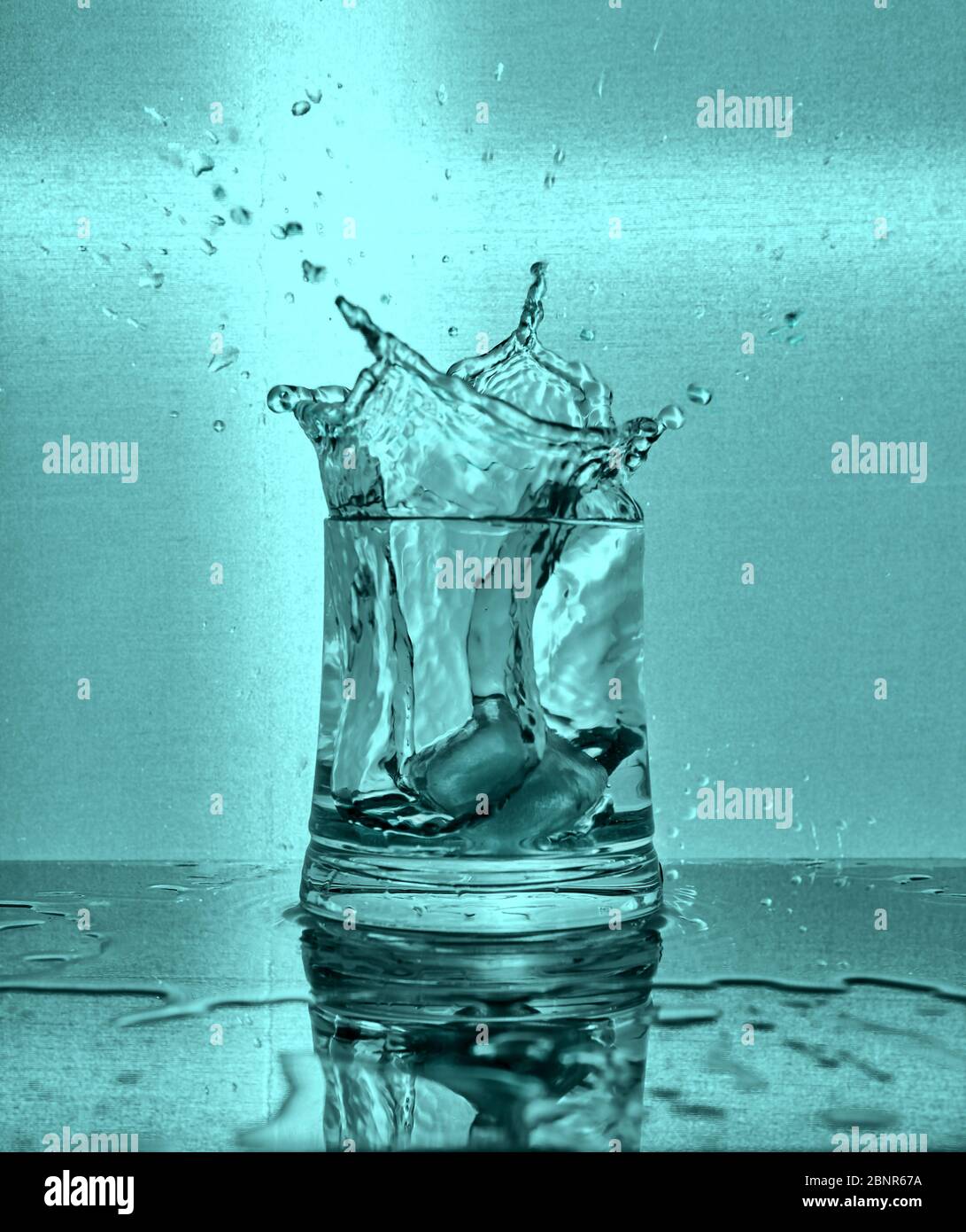 Ice cubes splashing into glass of water. Blue background Stock Photo ...