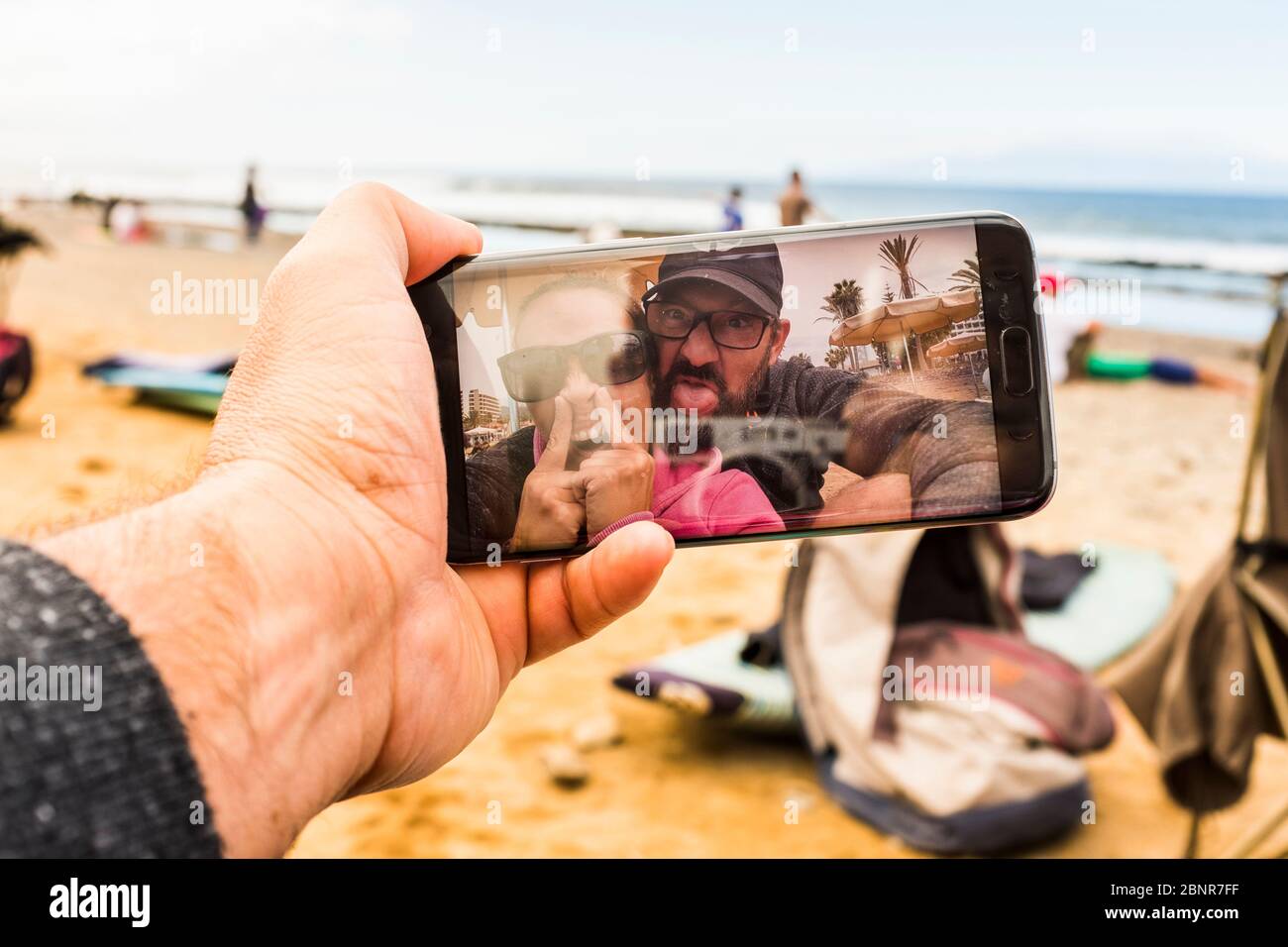 Couple of adult crazy man and woman in video call at the beach doing funny  expression - happy people with technology phone device making crazy - joy  and nice adults at the