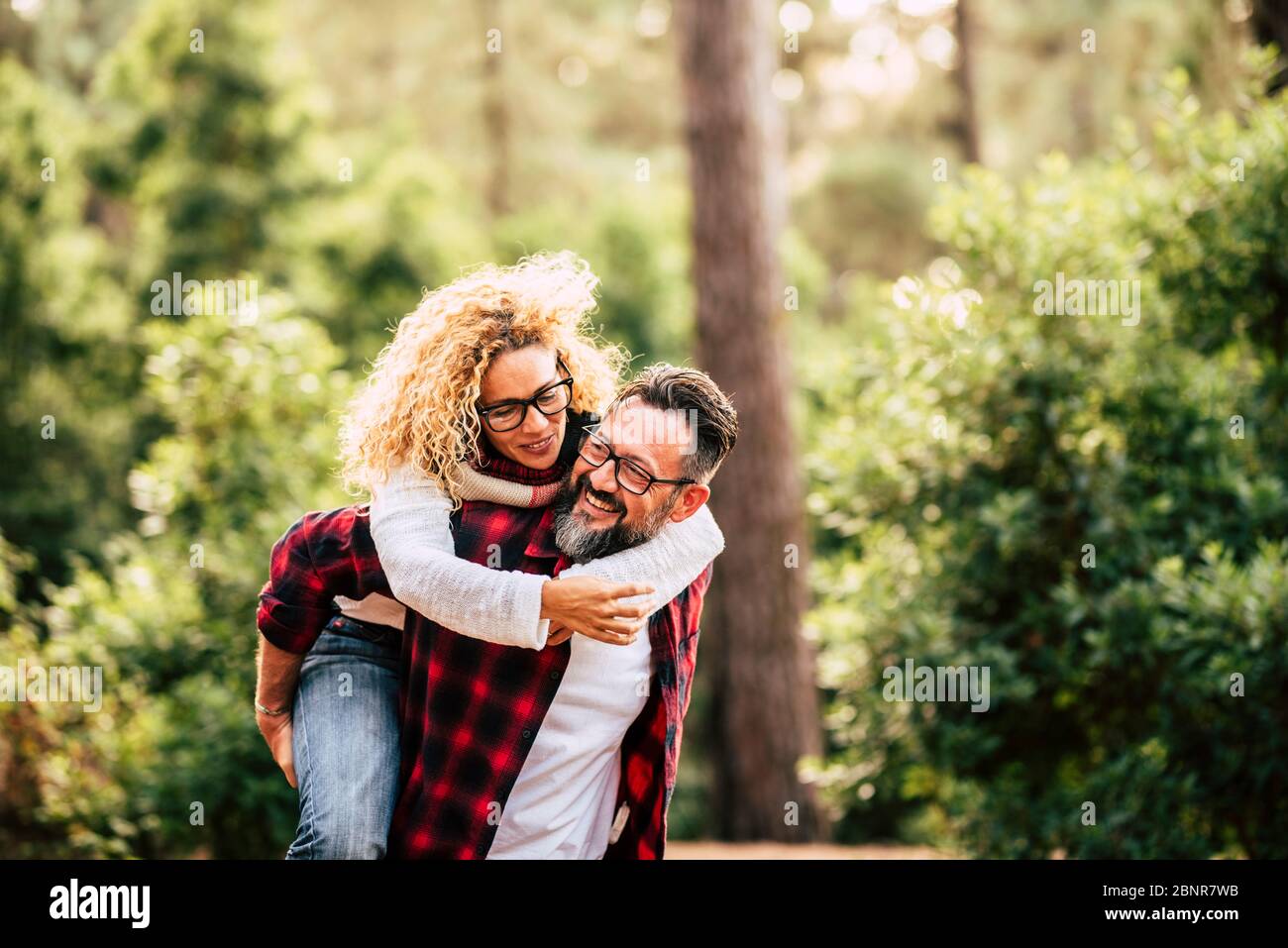 Happy adult caucasian couple in relationship and love play together in the forest wood nature - outdoor people leisure activity concept with cheerful caucasians Stock Photo
